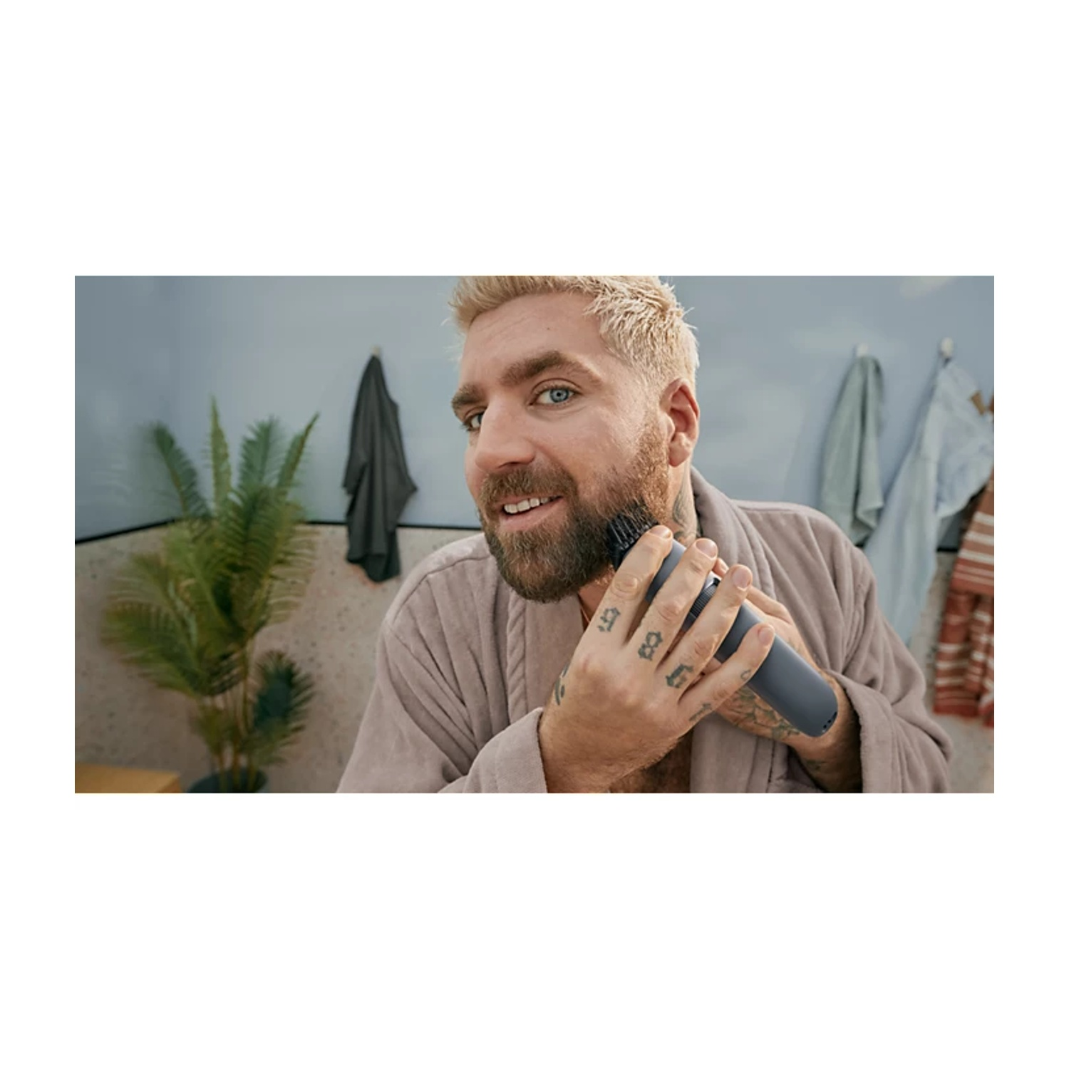 Un uomo con capelli biondi e barba si rade la barba con un trimmer scuro.