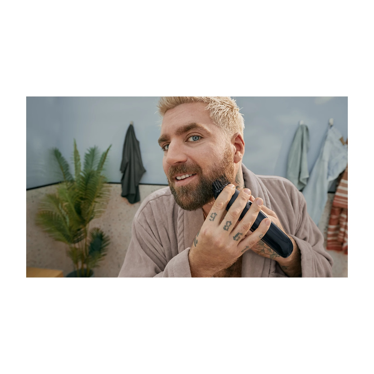 Uomo con capelli biondi e barba si rade la barba con un rifinitore nero.
