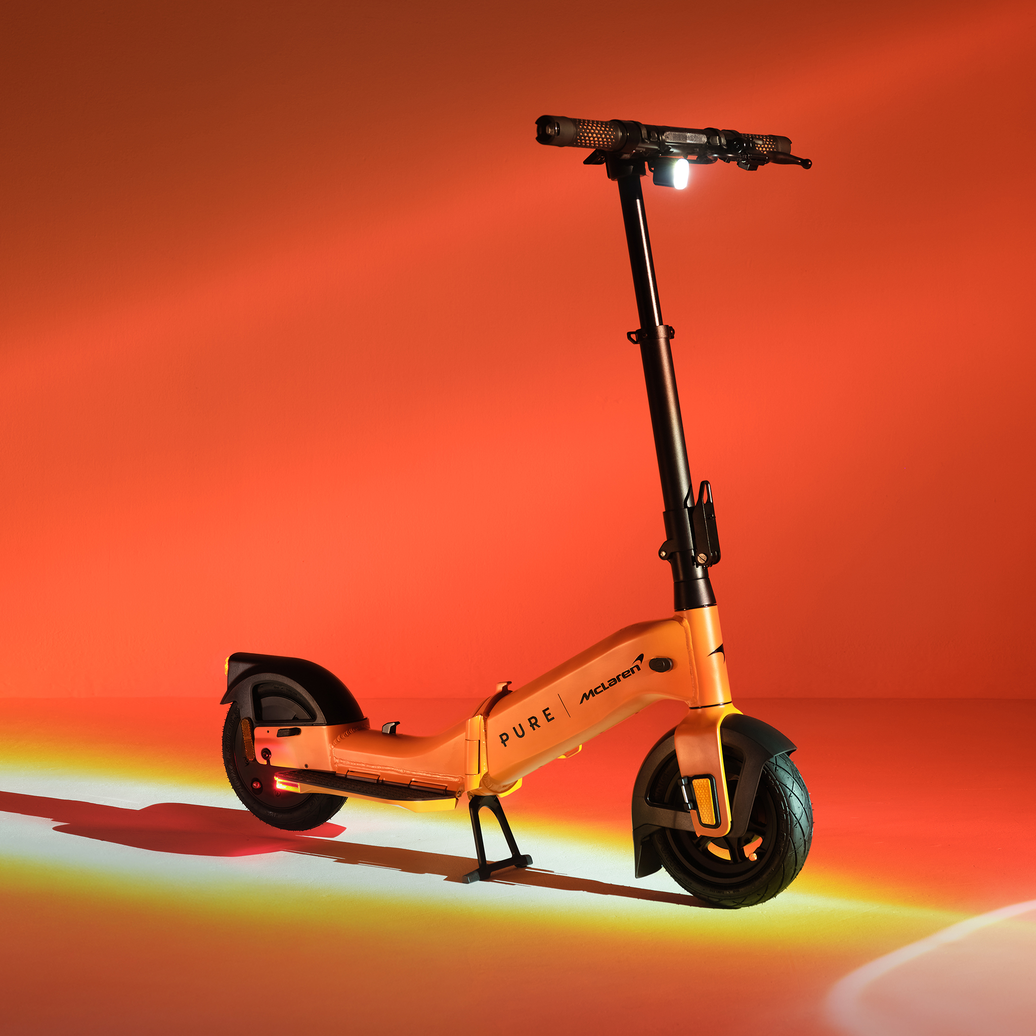 Ein orangefarbener E-Scooter mit McLaren-Logo, beleuchtet vor einem roten Hintergrund.