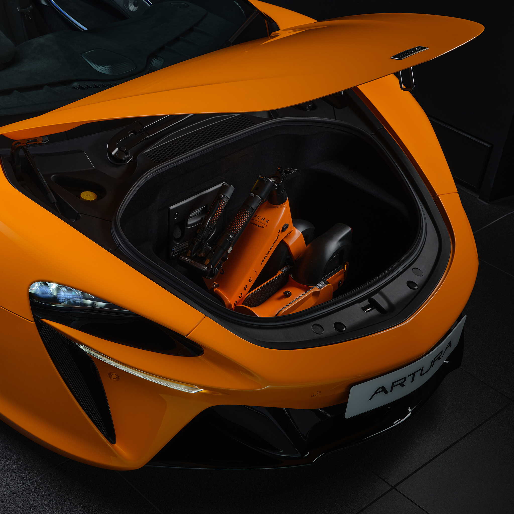 Ein orangefarbener McLaren mit offenem Kofferraum, darin ein zusammengeklappter E-Scooter.