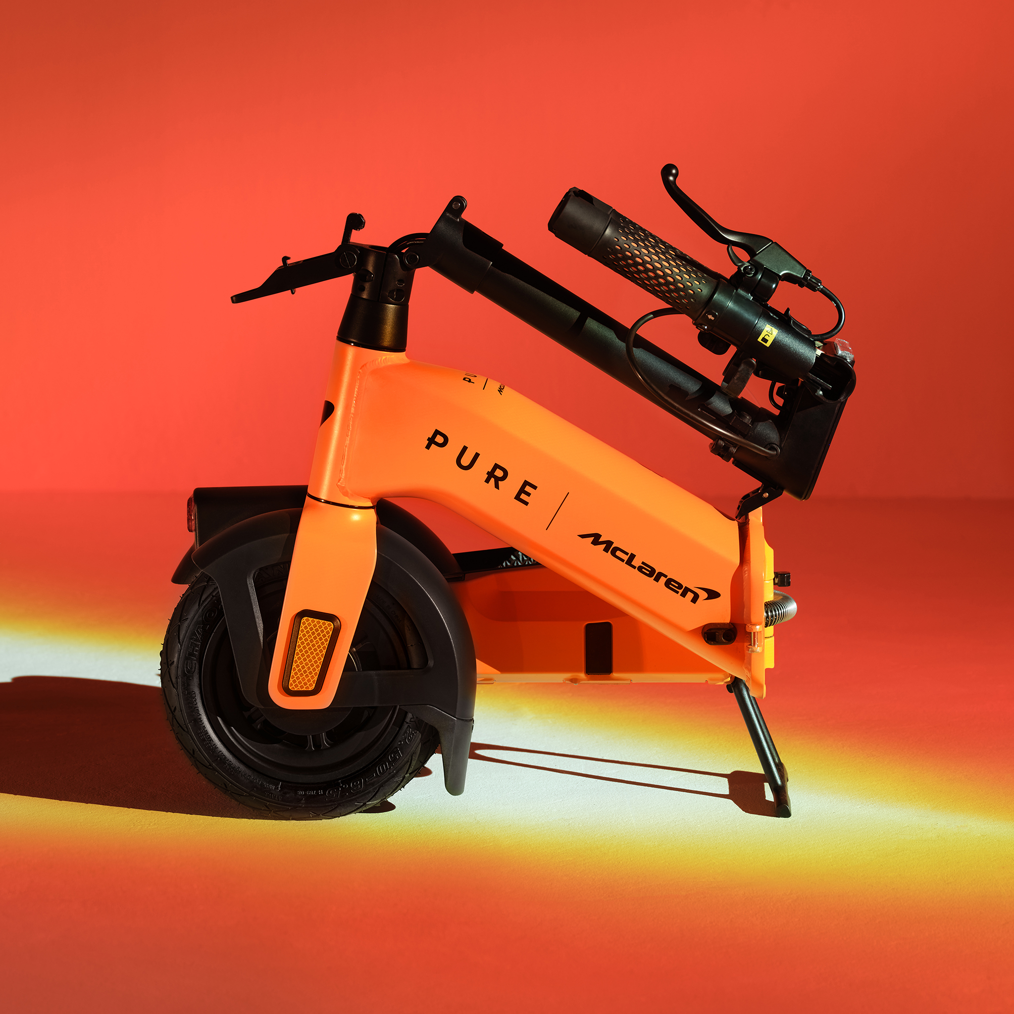 Ein orangefarbener E-Scooter mit McLaren-Branding steht vor einem roten Hintergrund.