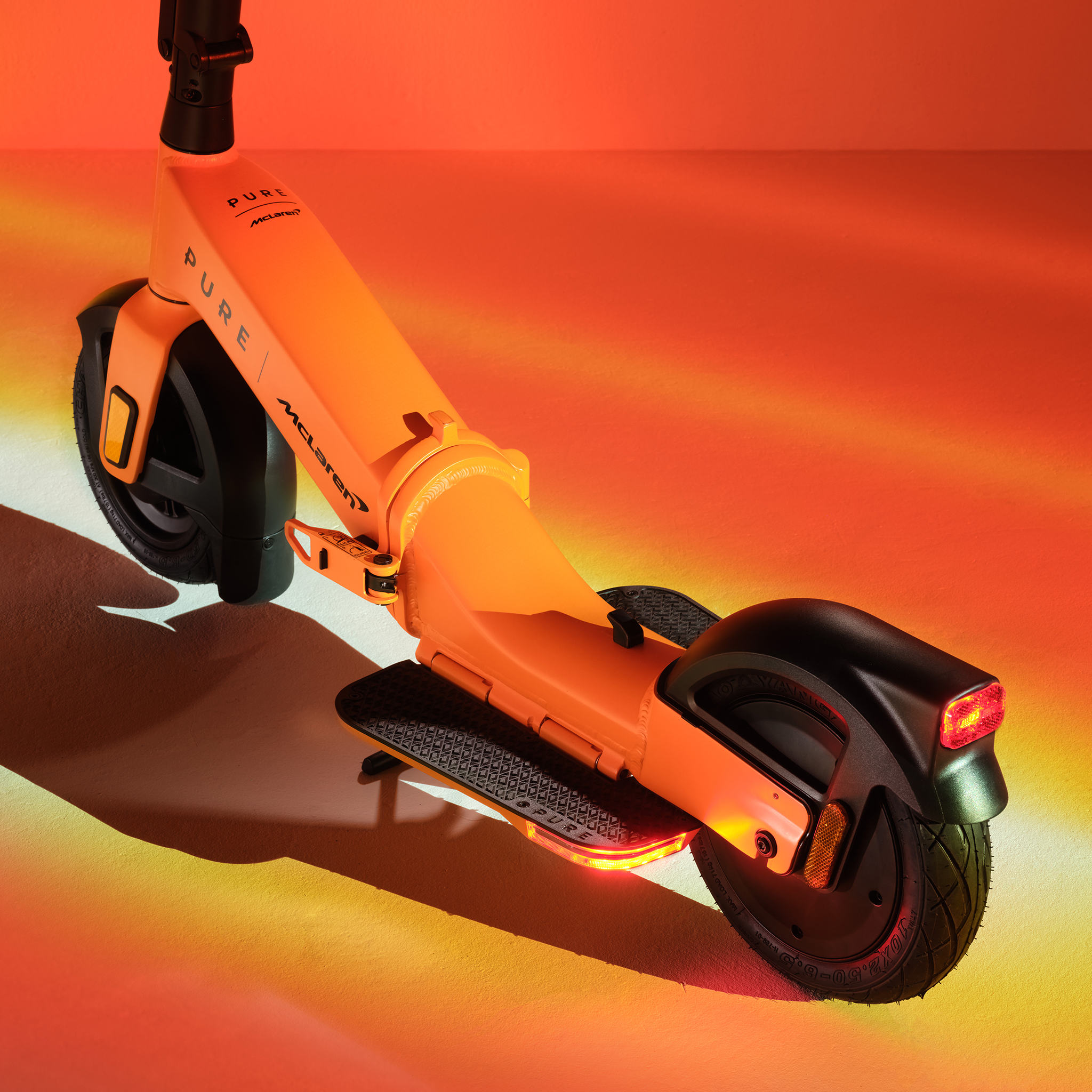 Orange E-Scooter mit McLaren-Logo im Detail, beleuchtet mit warmem Licht.