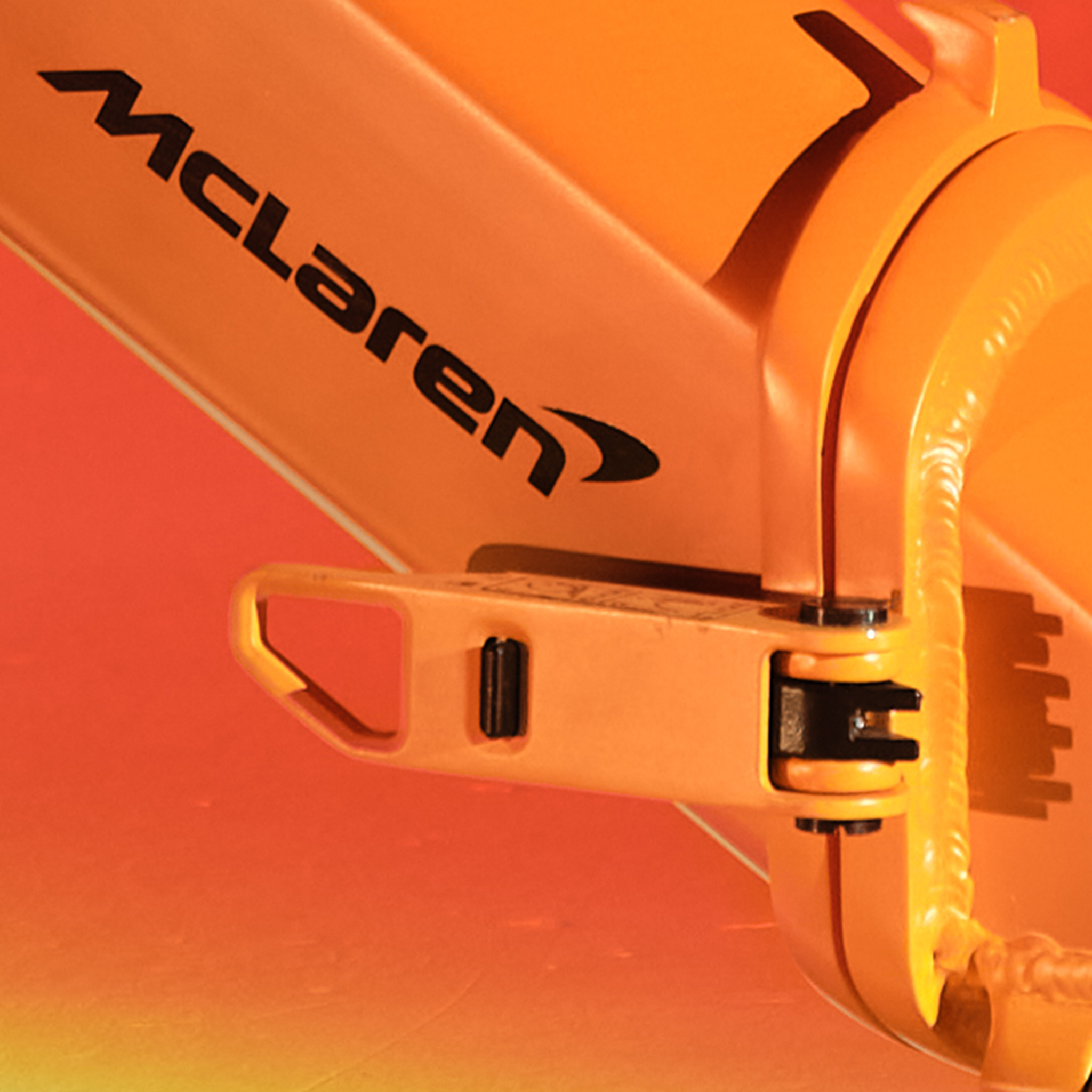 Orange McLaren-Logo auf einem Teil eines Fahrzeugs mit metallischen Verbindungsstücken.