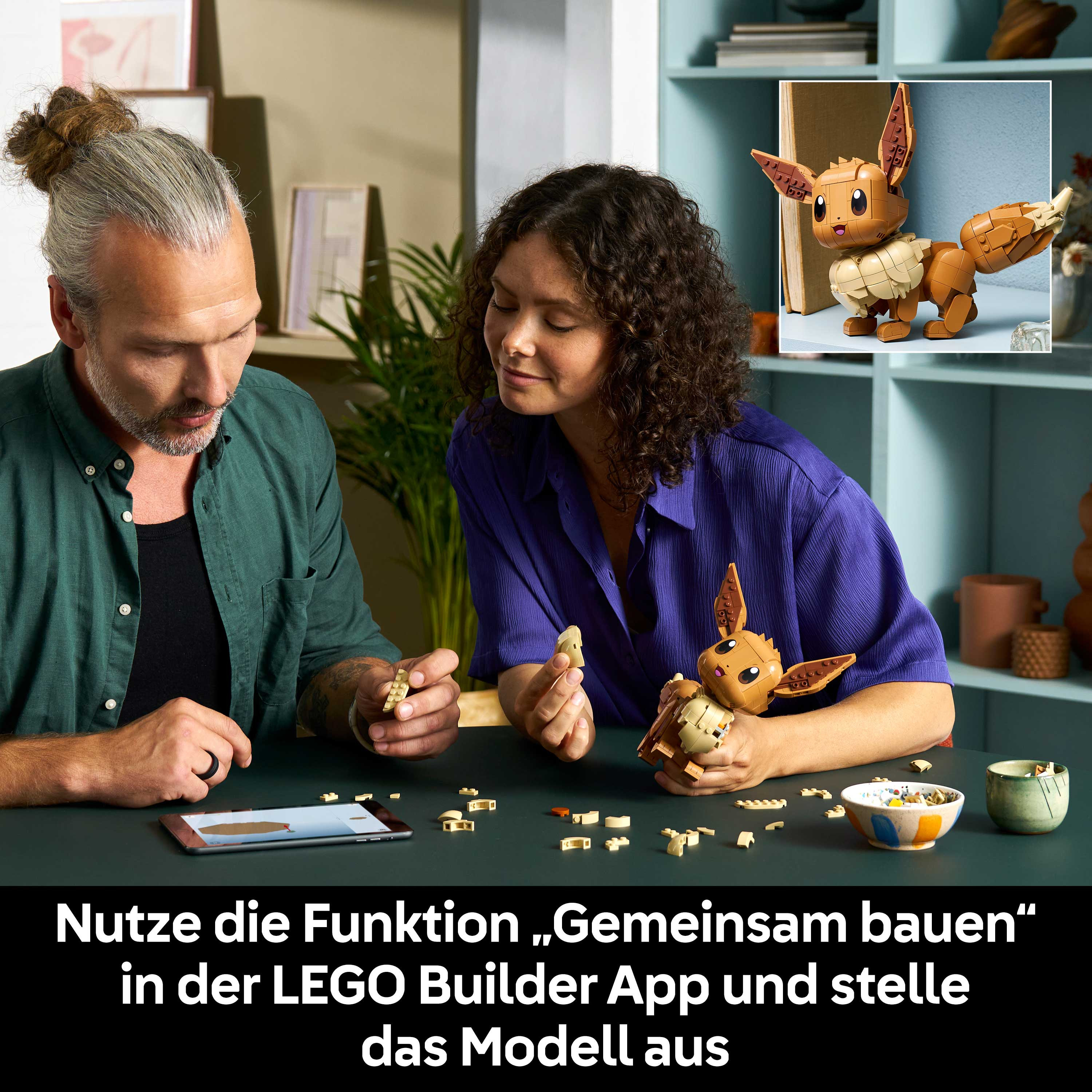 Zwei Personen bauen einen braunen LEGO Eevee-Charakter, während eine App auf einem Tablet angezeigt wird.