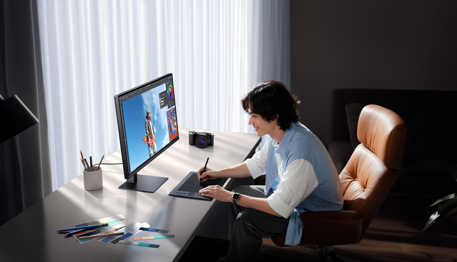 Un hombre se sienta en un escritorio usando una tableta gráfica. Un monitor muestra una imagen.
