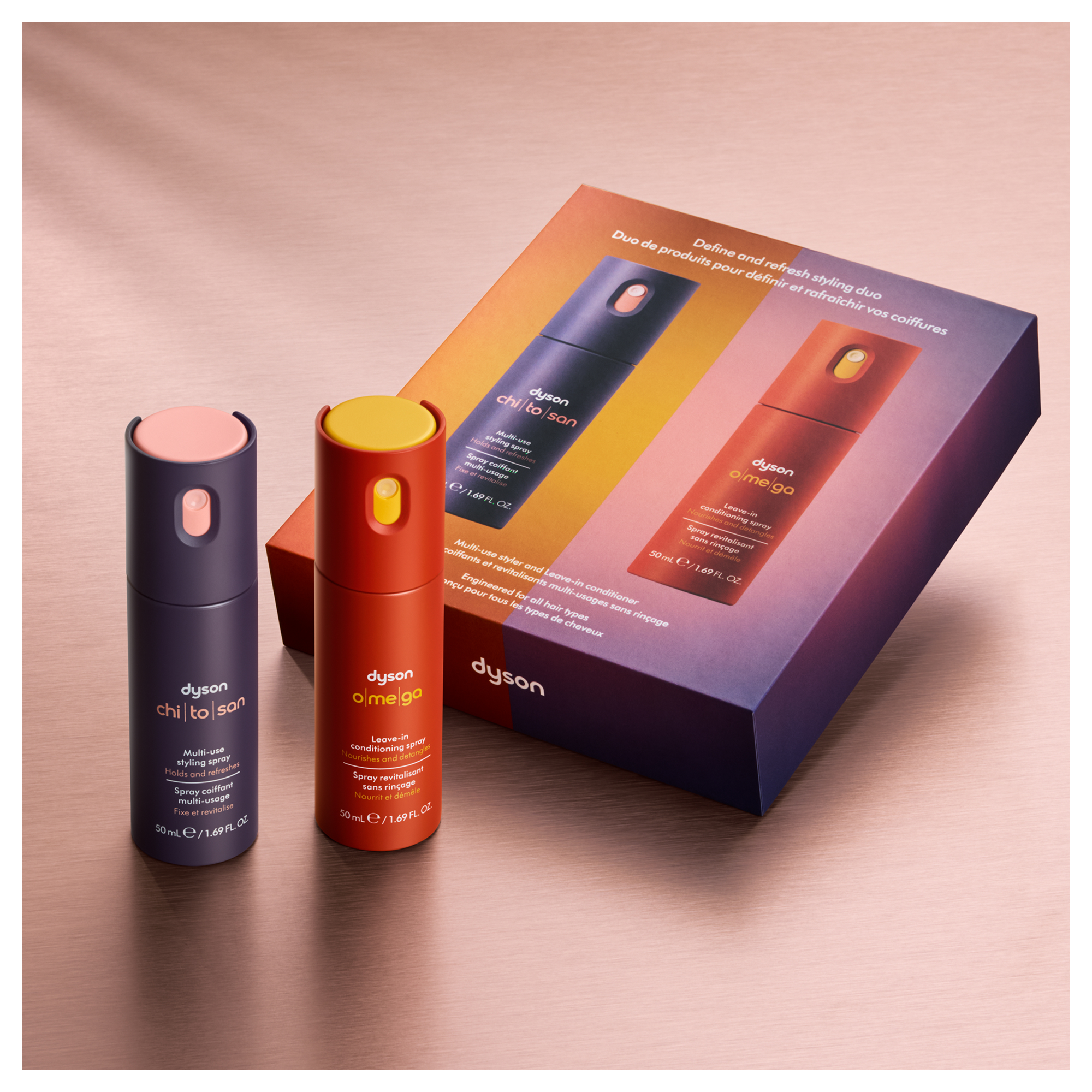 Zwei Dyson Stylingprodukte: blauer und oranger Sprühflakon auf pinker Unterlage.