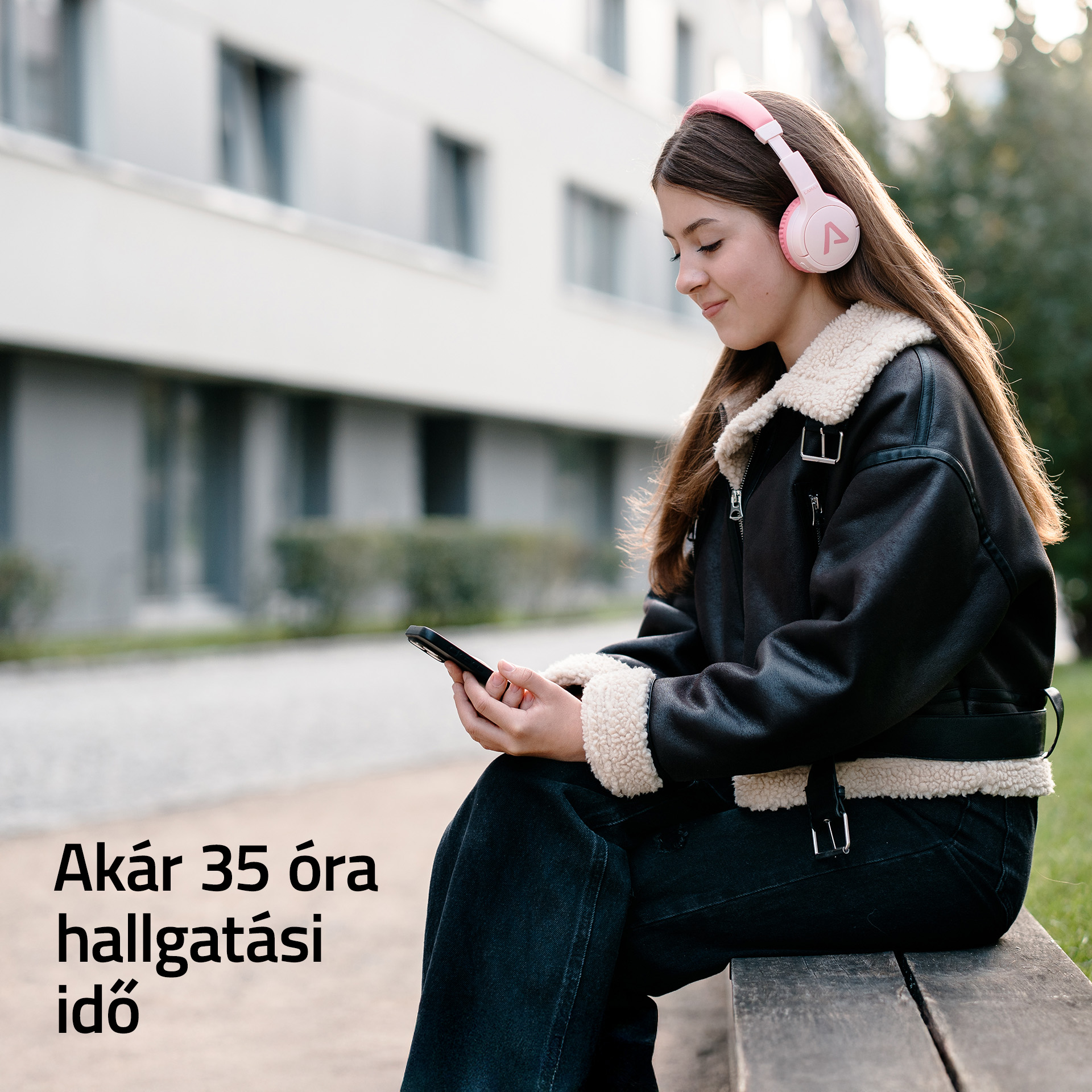 Egy lány rózsaszín fejhallgatóval ül kint, és a telefonját nézi.