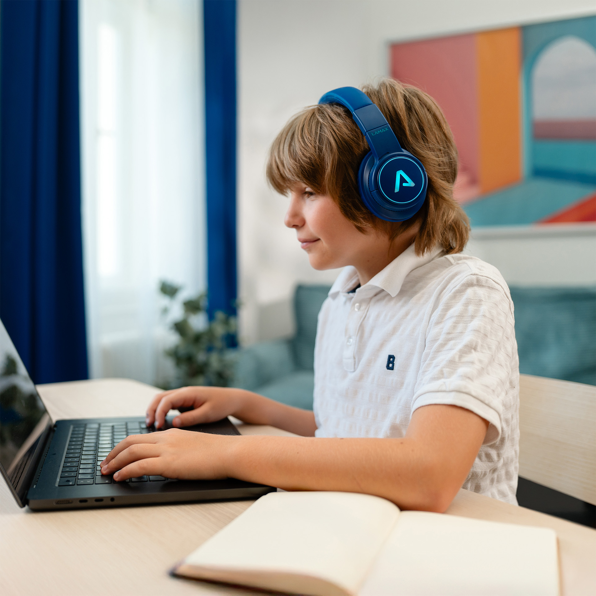 Fejhallgatós fiú gépel laptopon, mellette nyitott jegyzetfüzet.