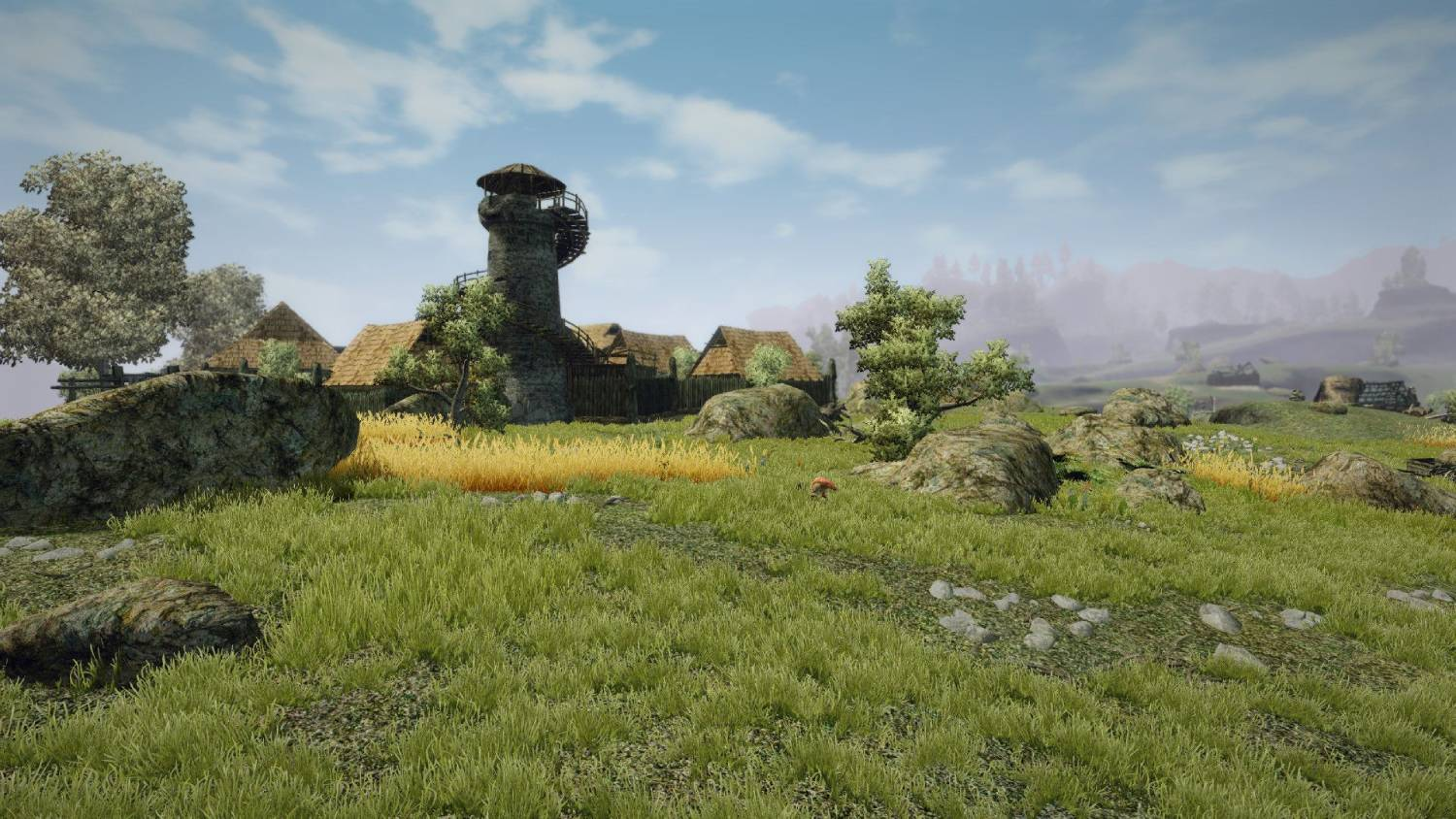 Una torre de piedra con escalera de caracol junto a colinas y casas.