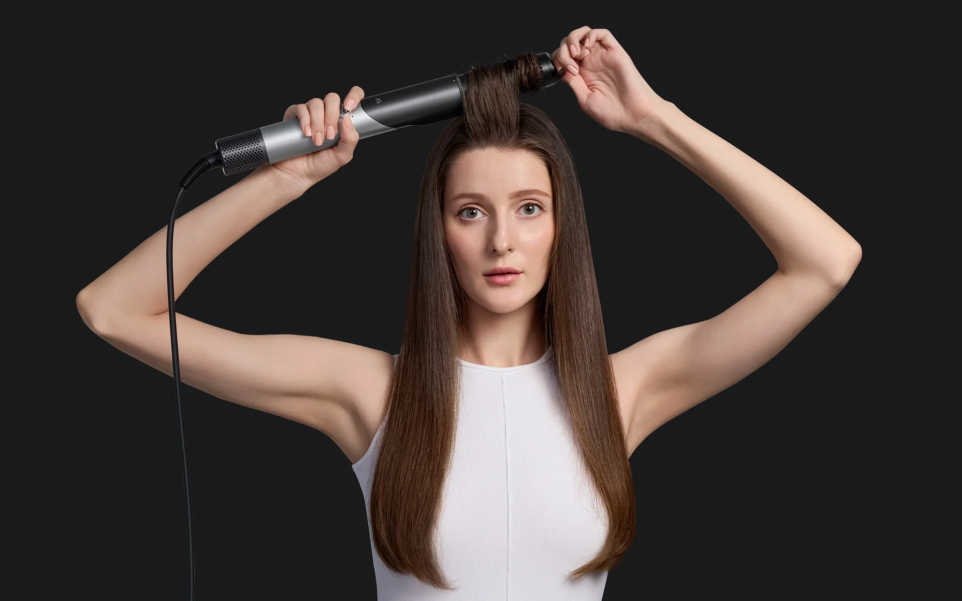Eine Frau mit langen braunen Haaren benutzt einen Lockenstab auf ihr Haar.