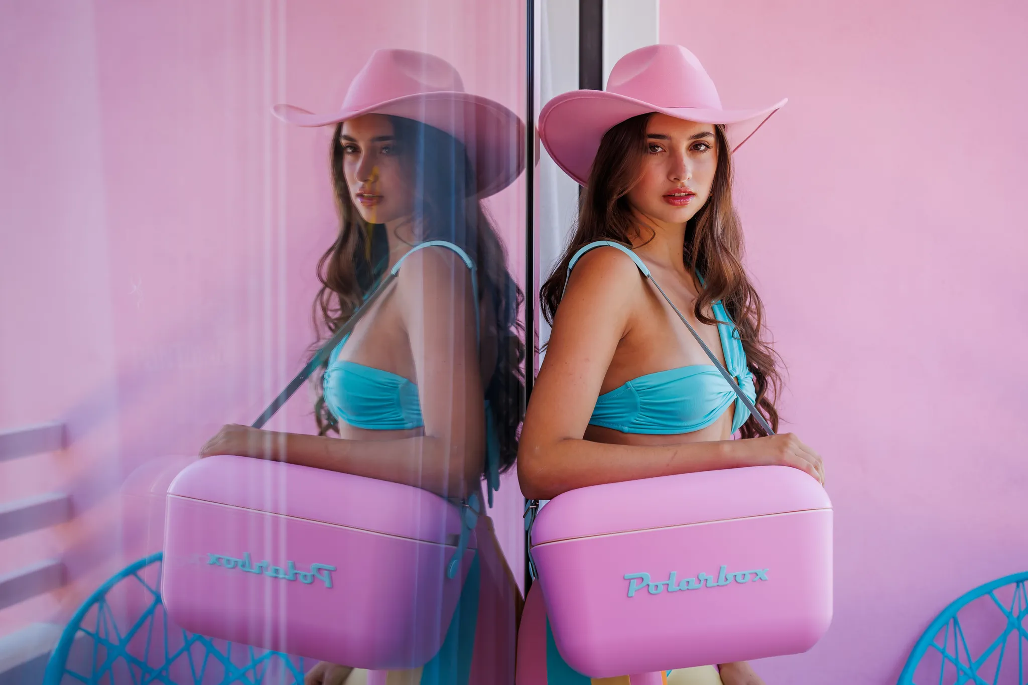 Una donna con cappello da cowboy rosa e bikini blu porta una borsa rosa.