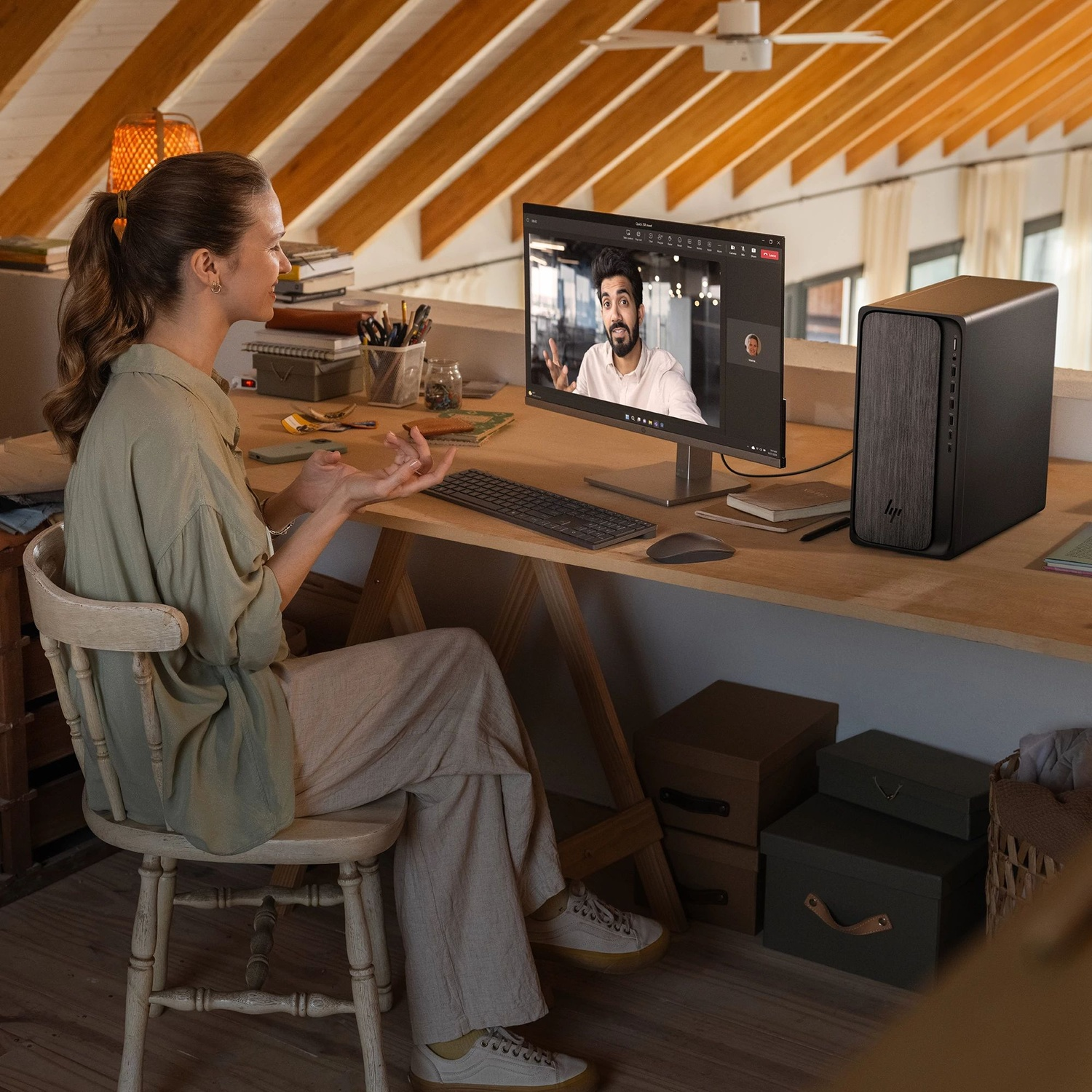A woman in loungewear video calls from an attic office, with a computer and desk.