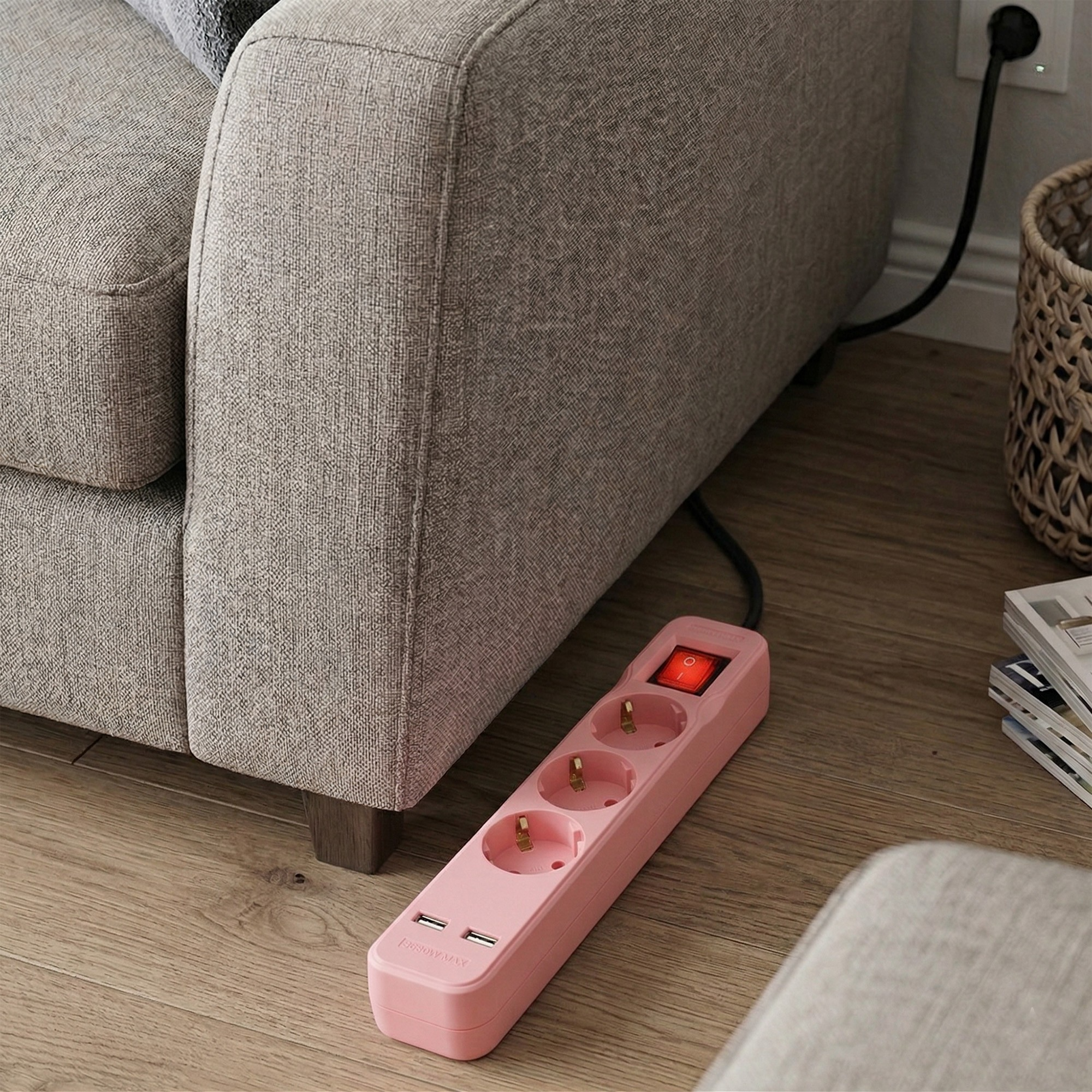 Egy rózsaszín elosztó kapcsolóval és USB-portokkal fekszik egy fa padlón egy kanapé mellett.