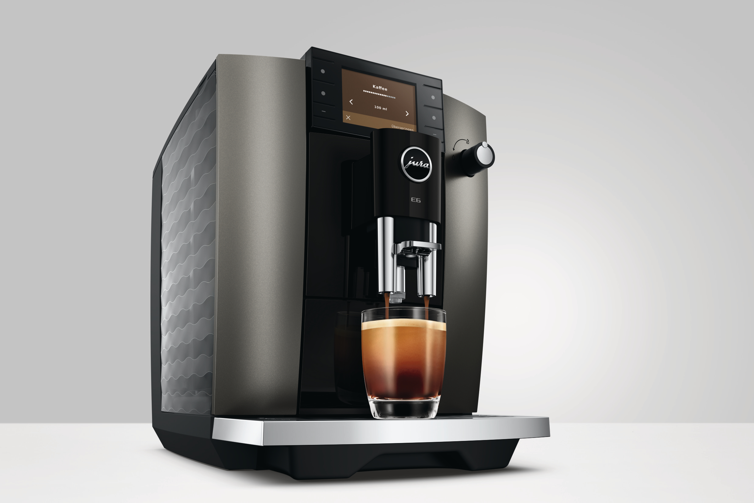 Eine JURA E6 Kaffeemaschine brüht Espresso in ein Glas auf einer weißen Oberfläche.