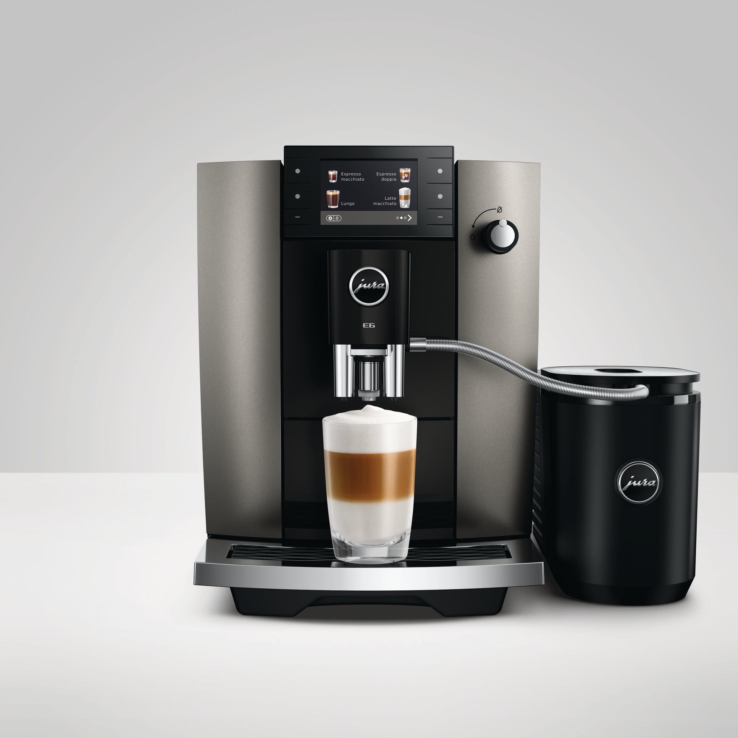Eine Jura Kaffeemaschine brüht einen Latte Macchiato in ein Glas, daneben ein Milchbehälter.
