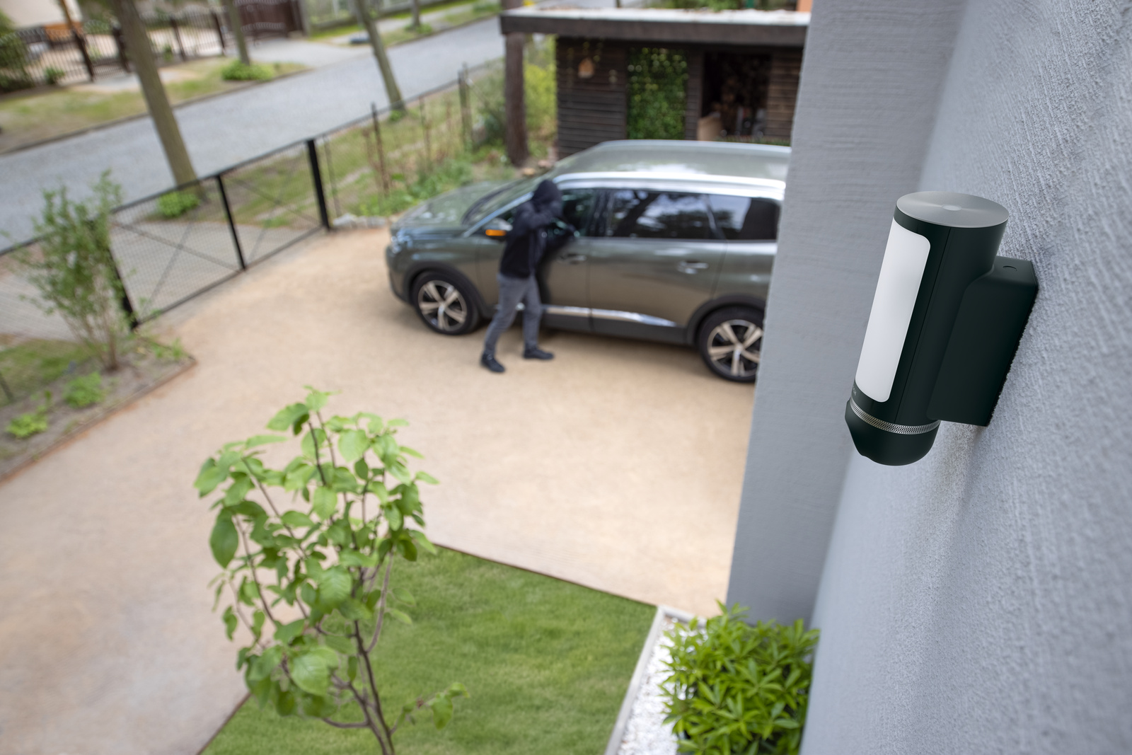 Ein Mann in dunkler Kleidung öffnet die Autotür neben einem Haus.