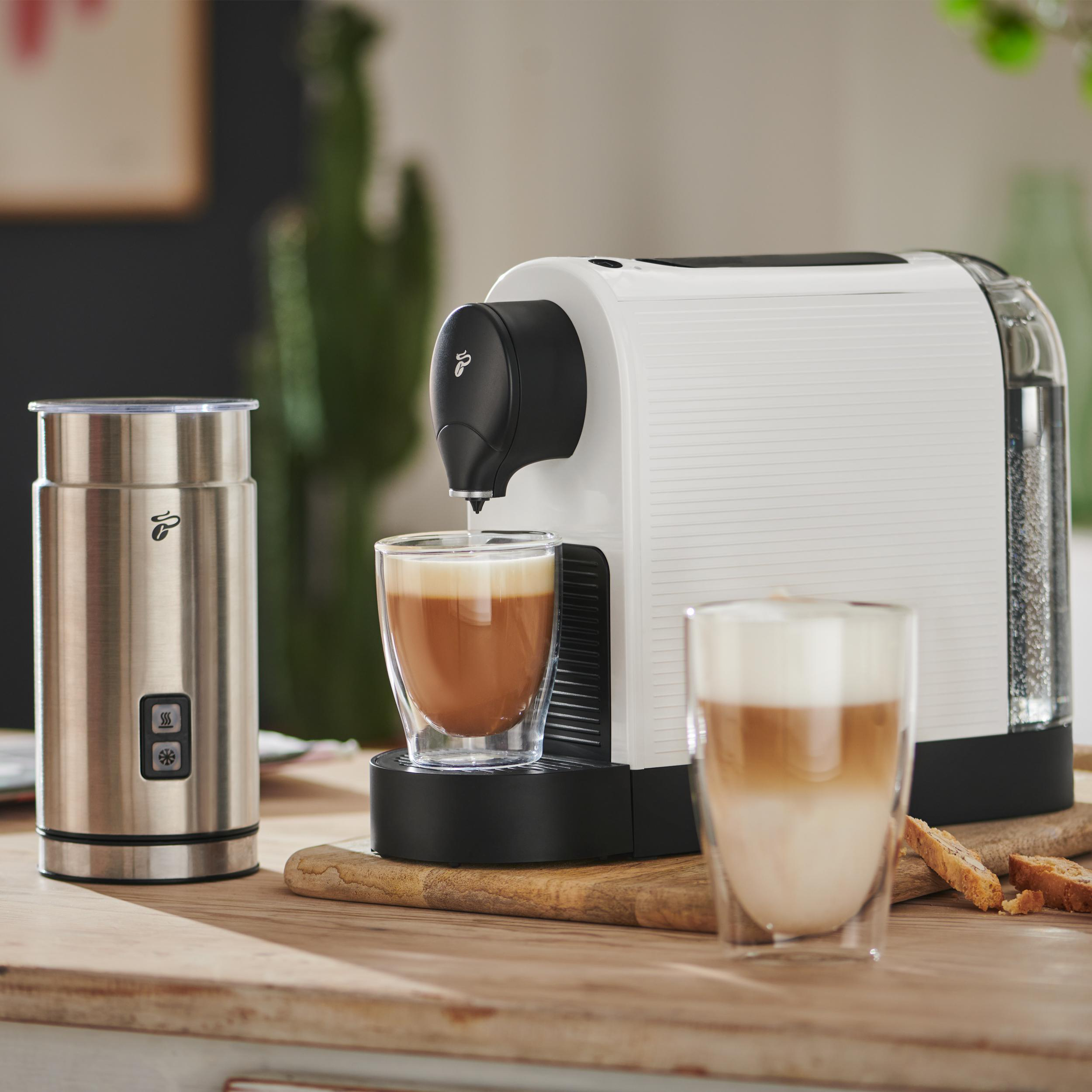 Eine weiße Kaffeemaschine mit Milchaufschäumer und zwei Gläsern Kaffee auf einem Holztisch.