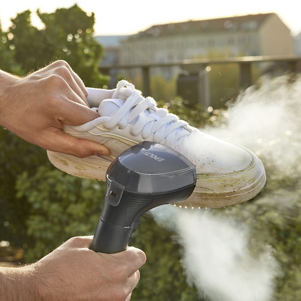 Manos limpiando zapatillas blancas con un limpiador a vapor en un balcón.