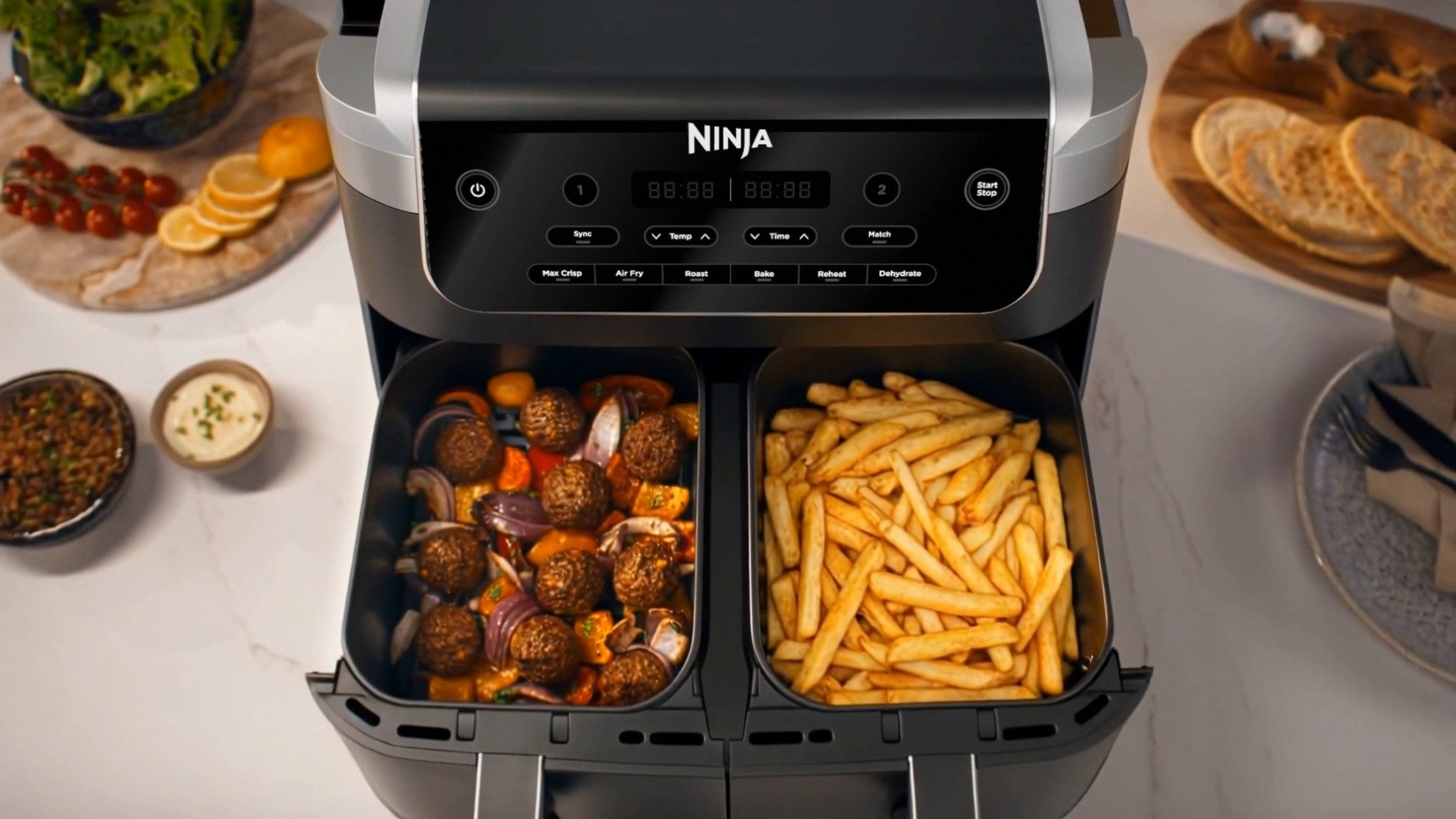 Freidora de aire doble con albóndigas y verduras en un cajón, papas fritas en el otro.