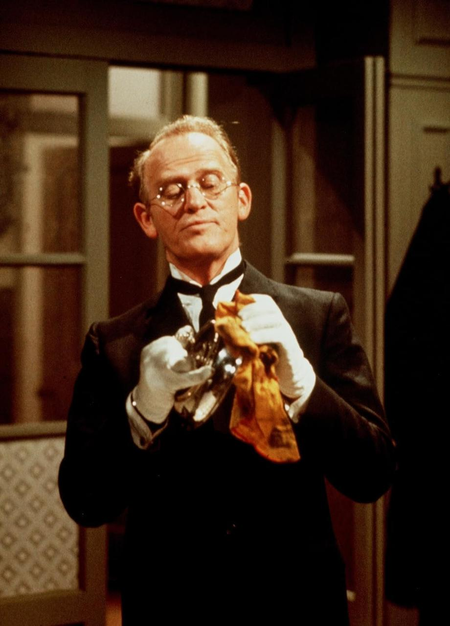 Ein Mann im Smoking mit Brille poliert Silber mit einem orangen Tuch.