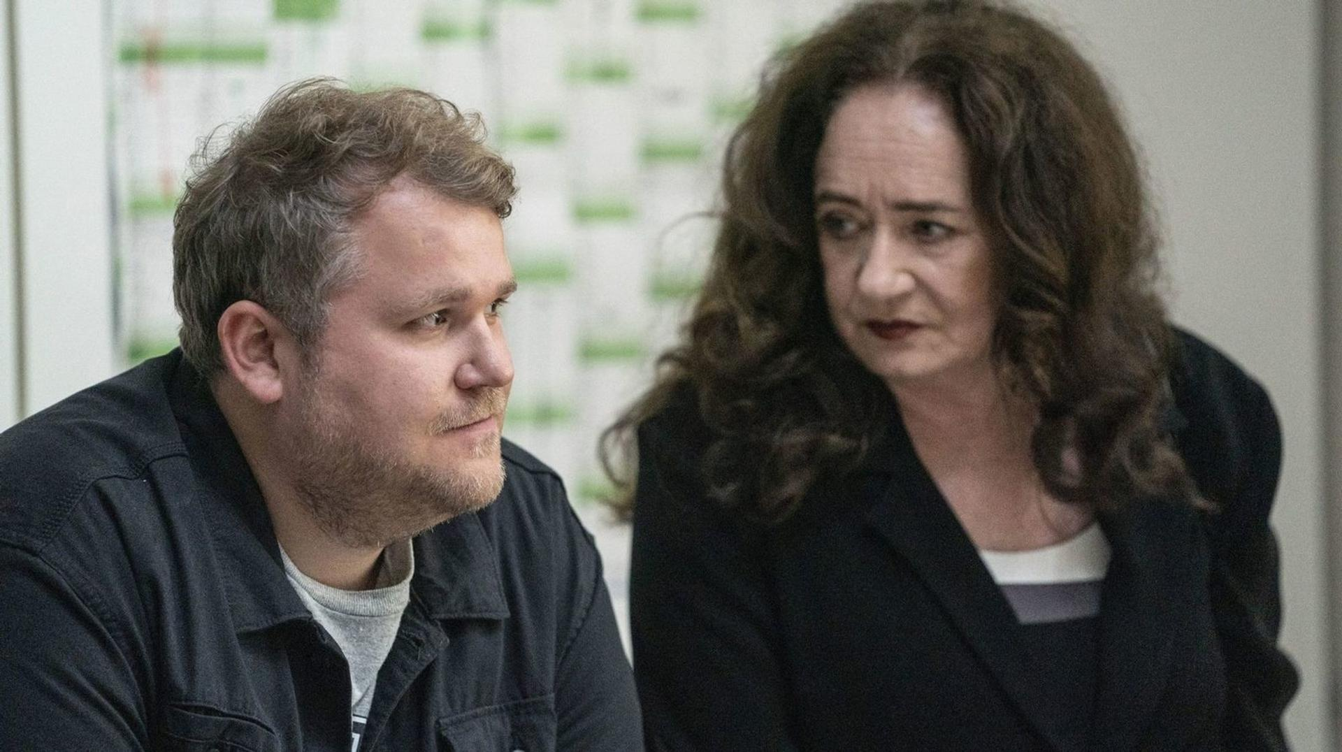 Ein Mann mit braunen Haaren und ein Frau mit langen braunen Haaren sitzen nebeneinander.