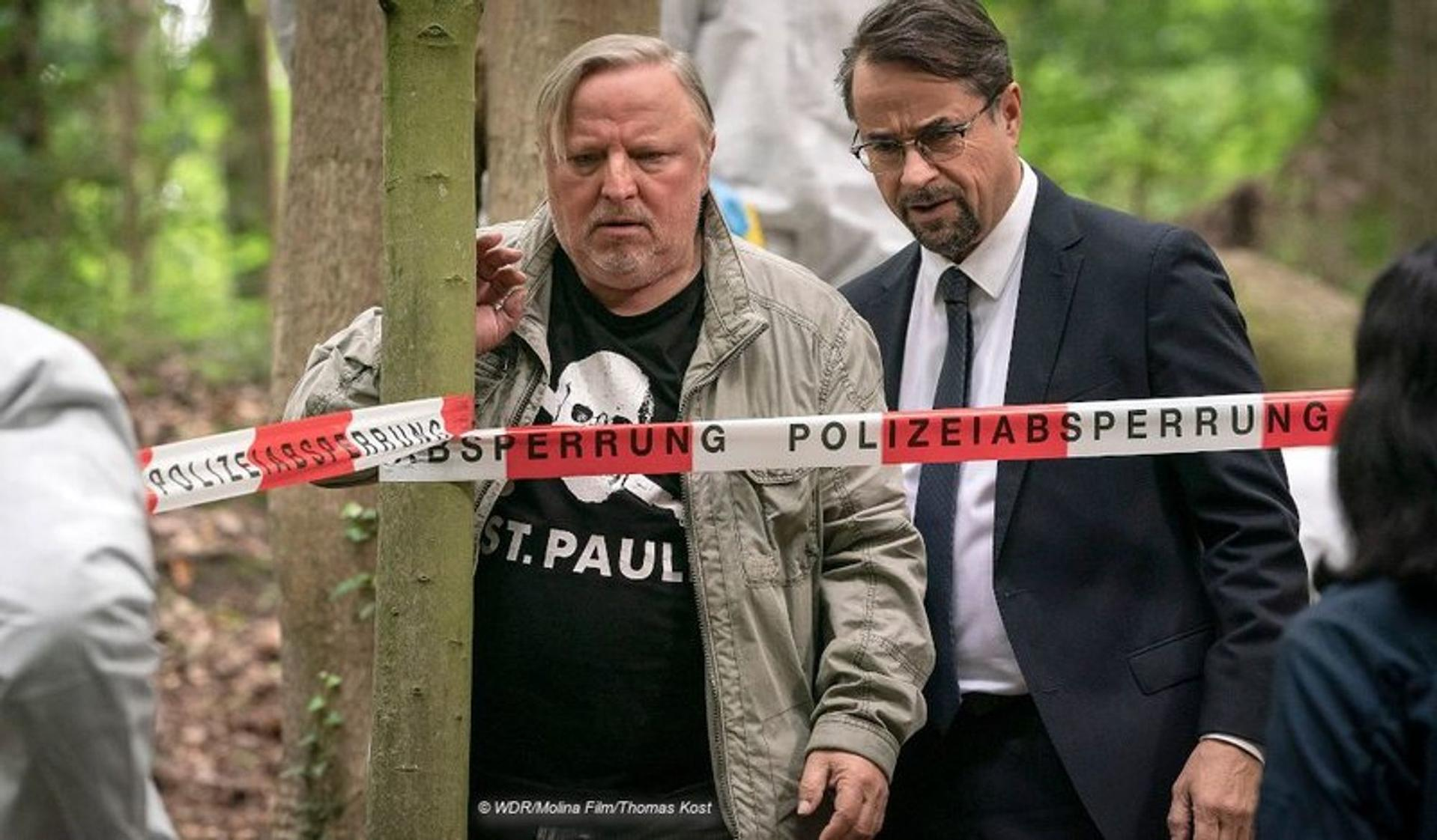 Zwei Männer stehen hinter Absperrband der Polizei in einem Wald.