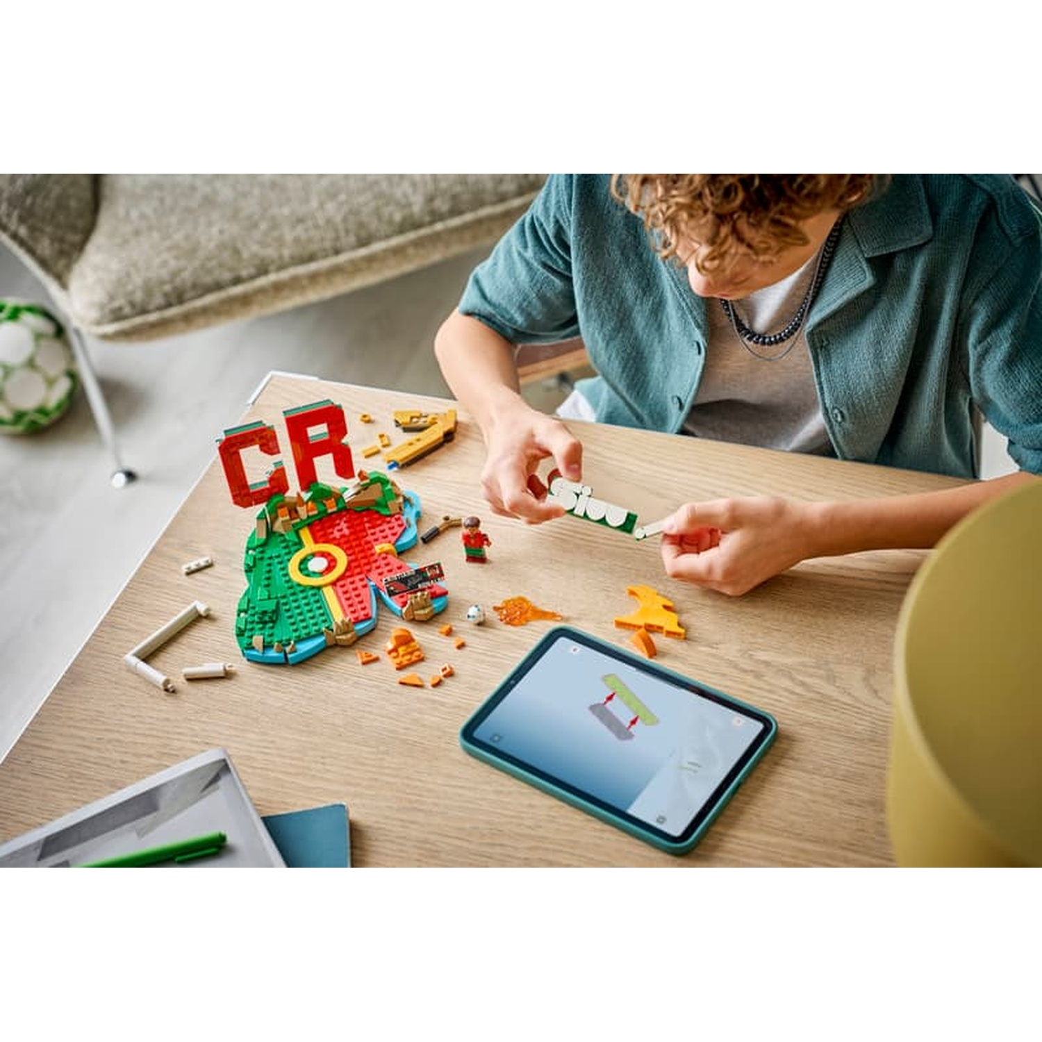 A boy builds with colorful LEGO bricks at a table, following instructions on a tablet.