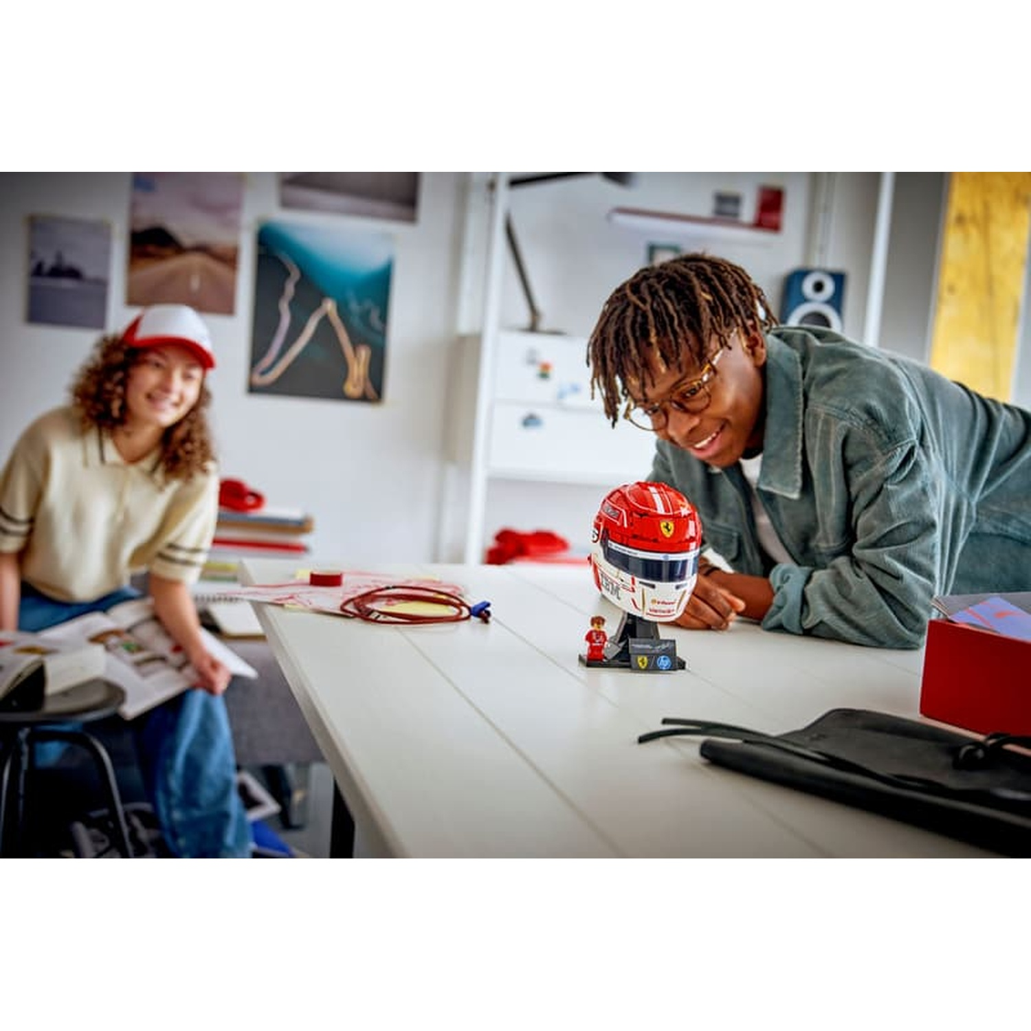 Two teens look at a Lego Ferrari helmet on a table. One smiles at the camera.