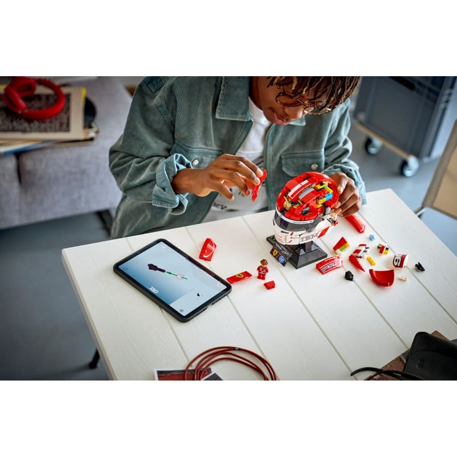 Young person building a Lego helmet, tablet nearby. Pieces on table.