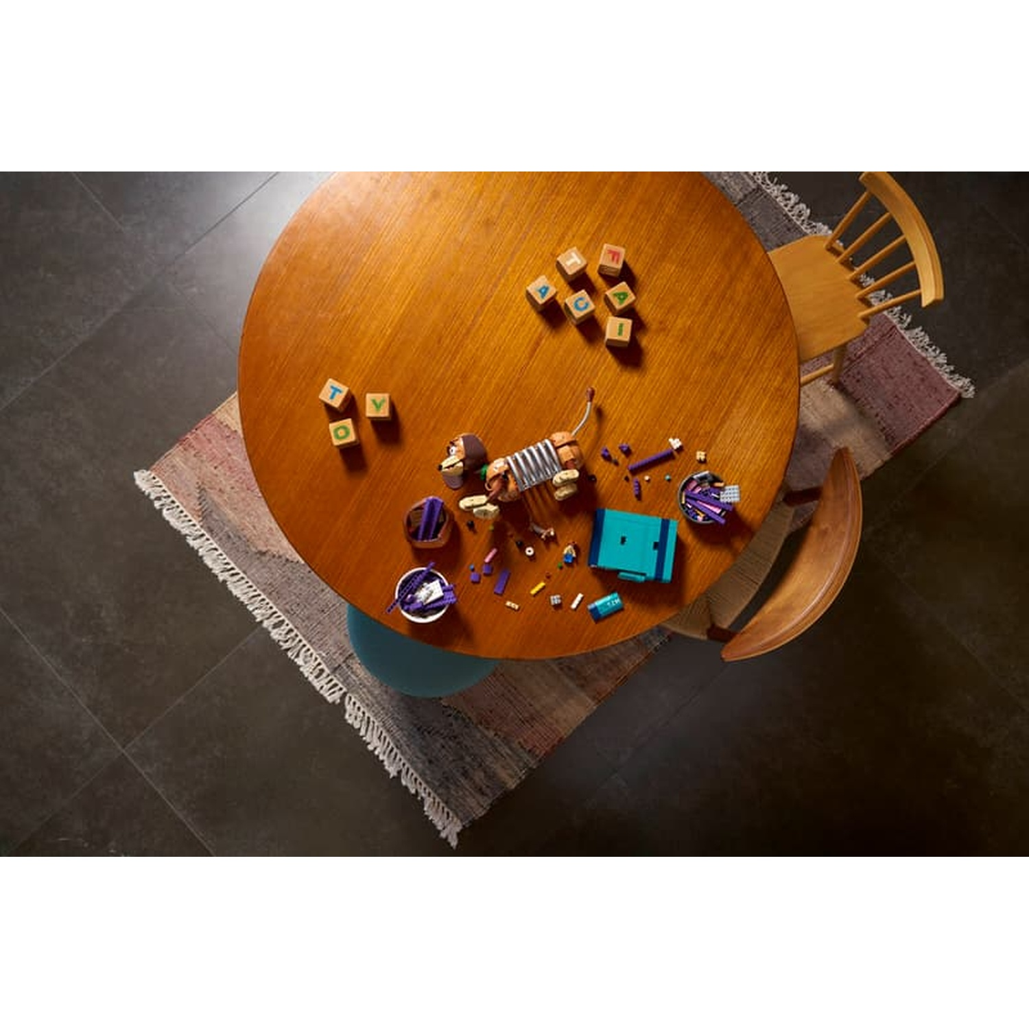 Houten tafel met speelgoed: blokken met letters, speelgoedhond en LEGO-onderdelen verspreid.