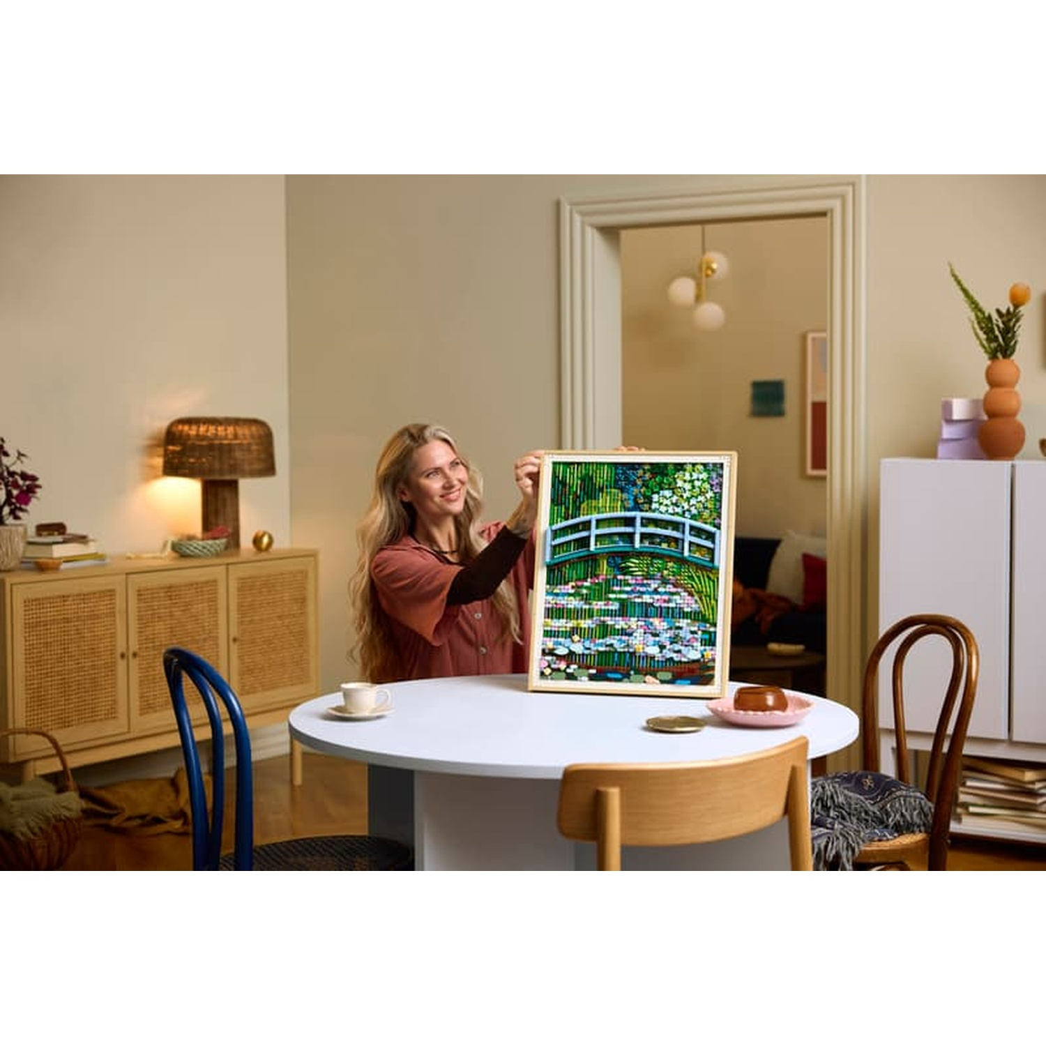 Woman holds up Monet's water lily painting. A table with a cup and cake.