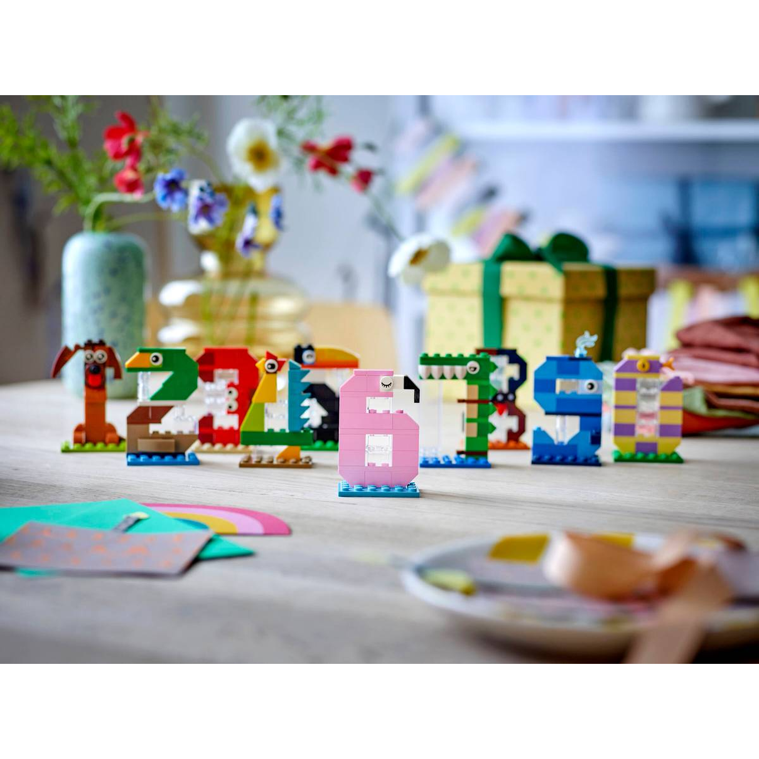 LEGO-cijfers 1-9 zijn als dieren gebouwd. Op de achtergrond staan bloemen en een cadeau.