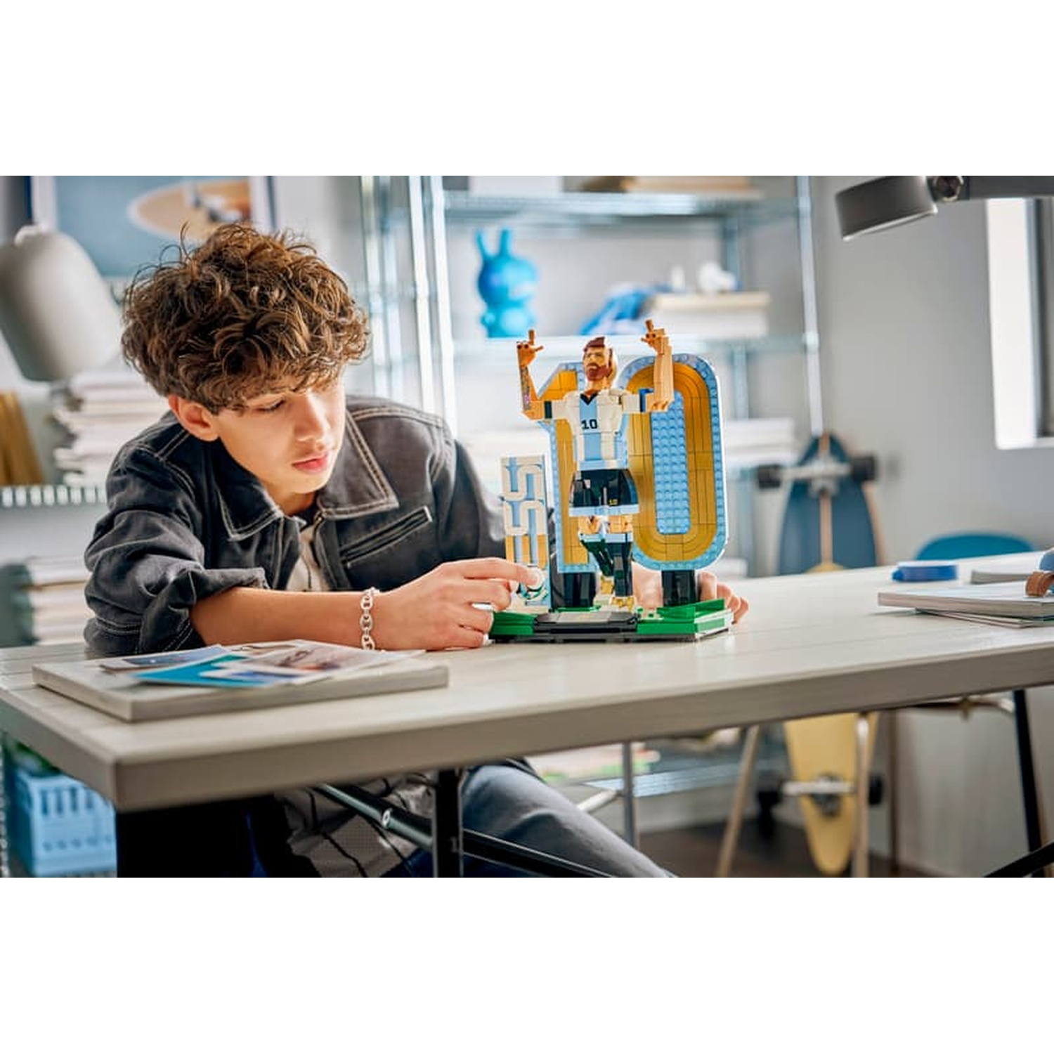 A boy builds a Lego figure of a soccer player at a desk.
