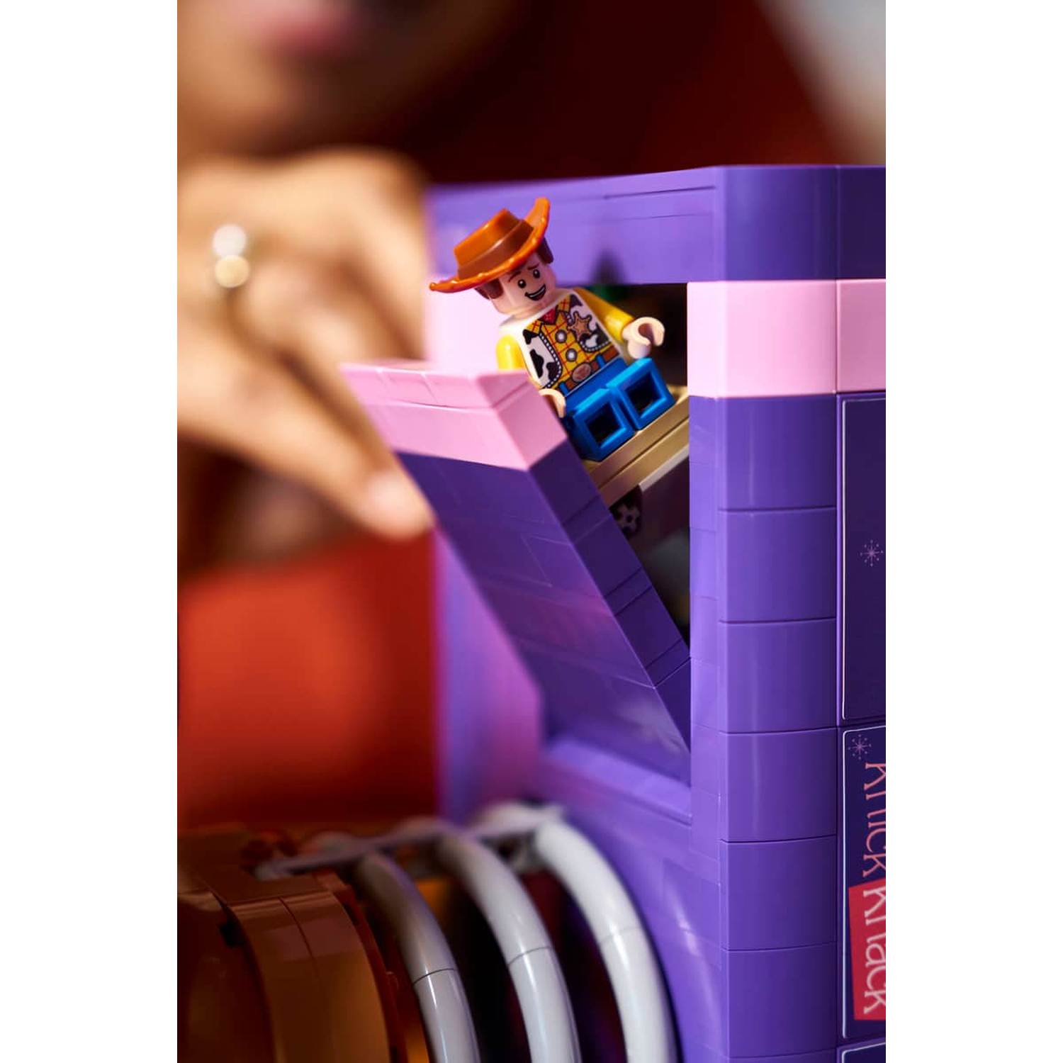 Een Lego Woody figuur met hoed staat op een paarse doos met roze accenten.