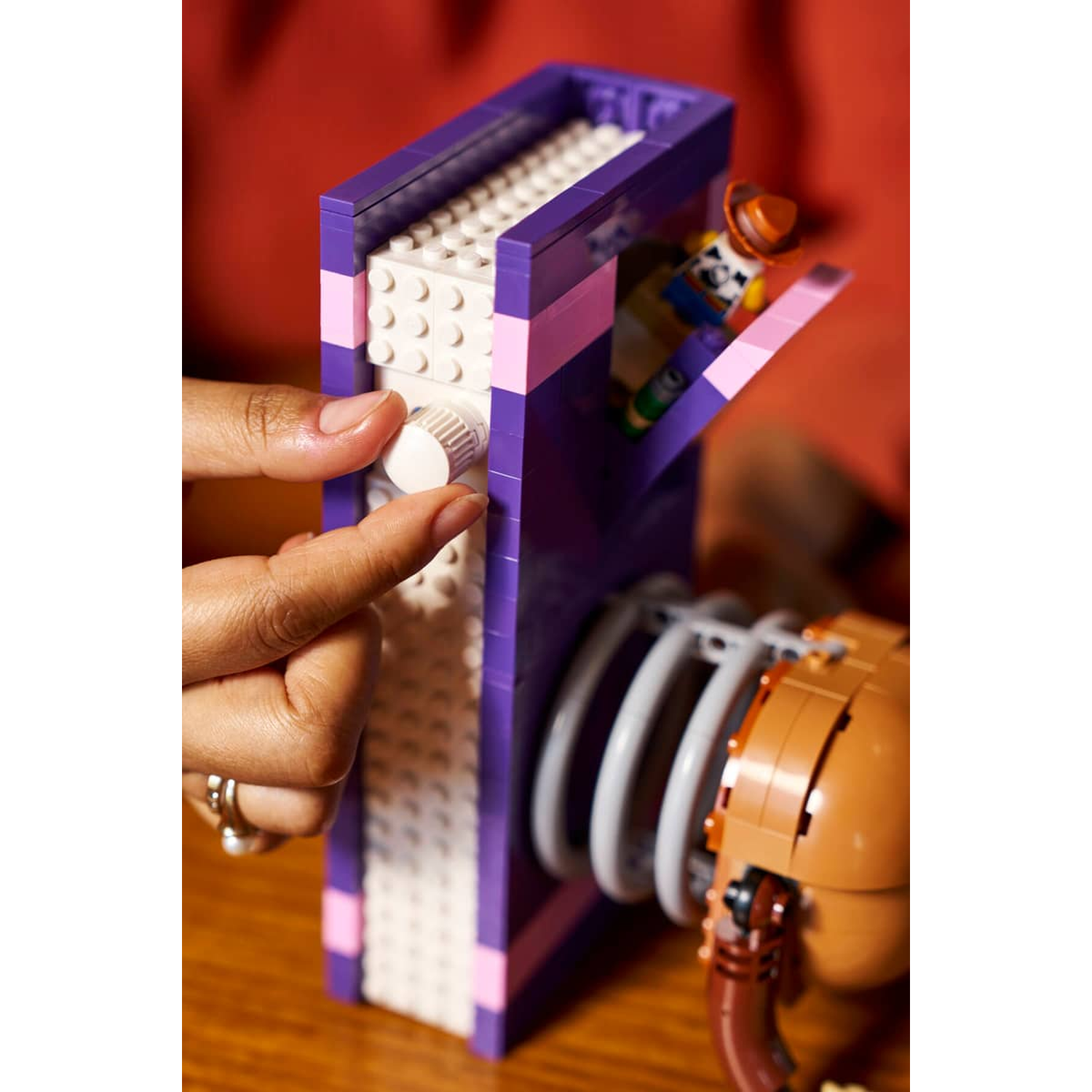 Een hand draait aan een knop op een paars Lego-boek met een figuur erin.