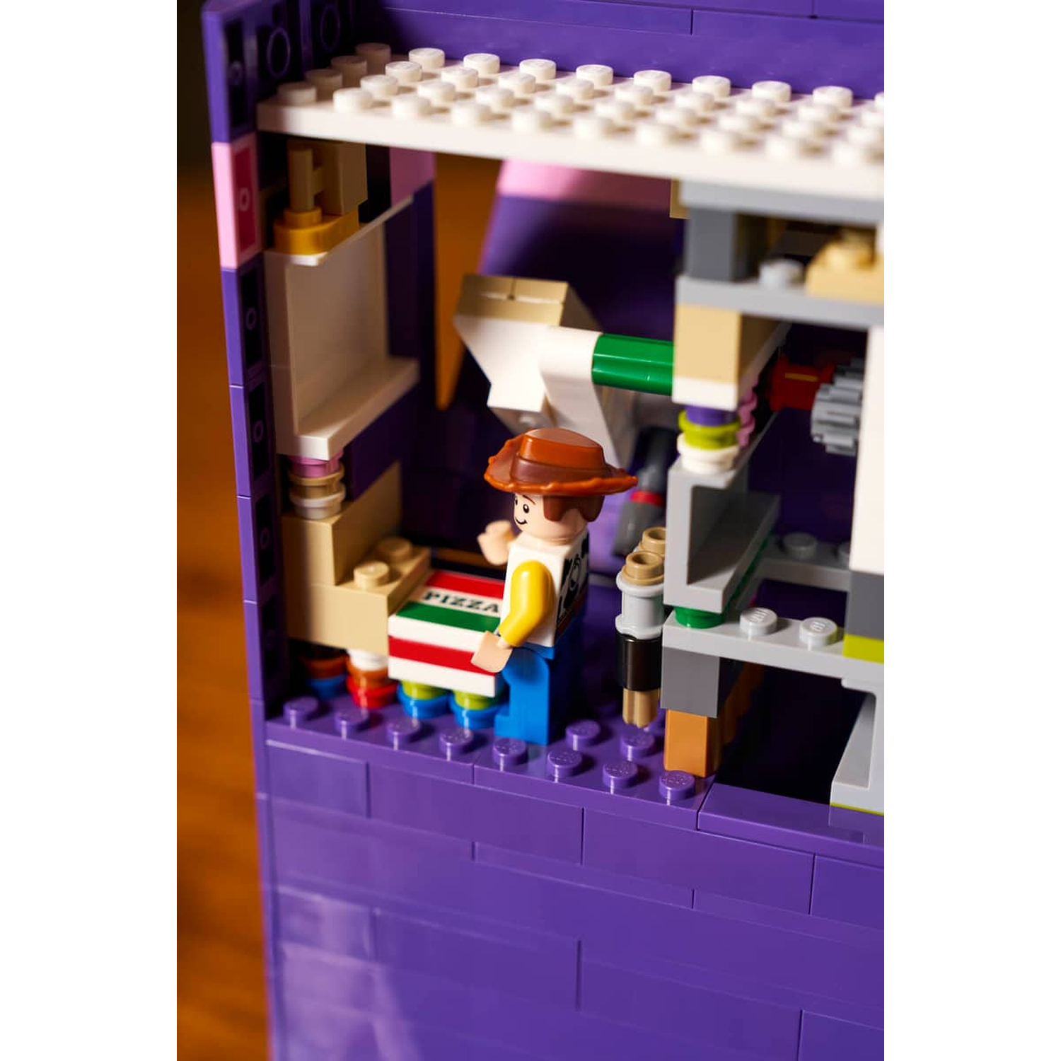 Een Lego-figuur met hoed die een pizzadoos vasthoudt, staat in een paars Lego-gebouw.