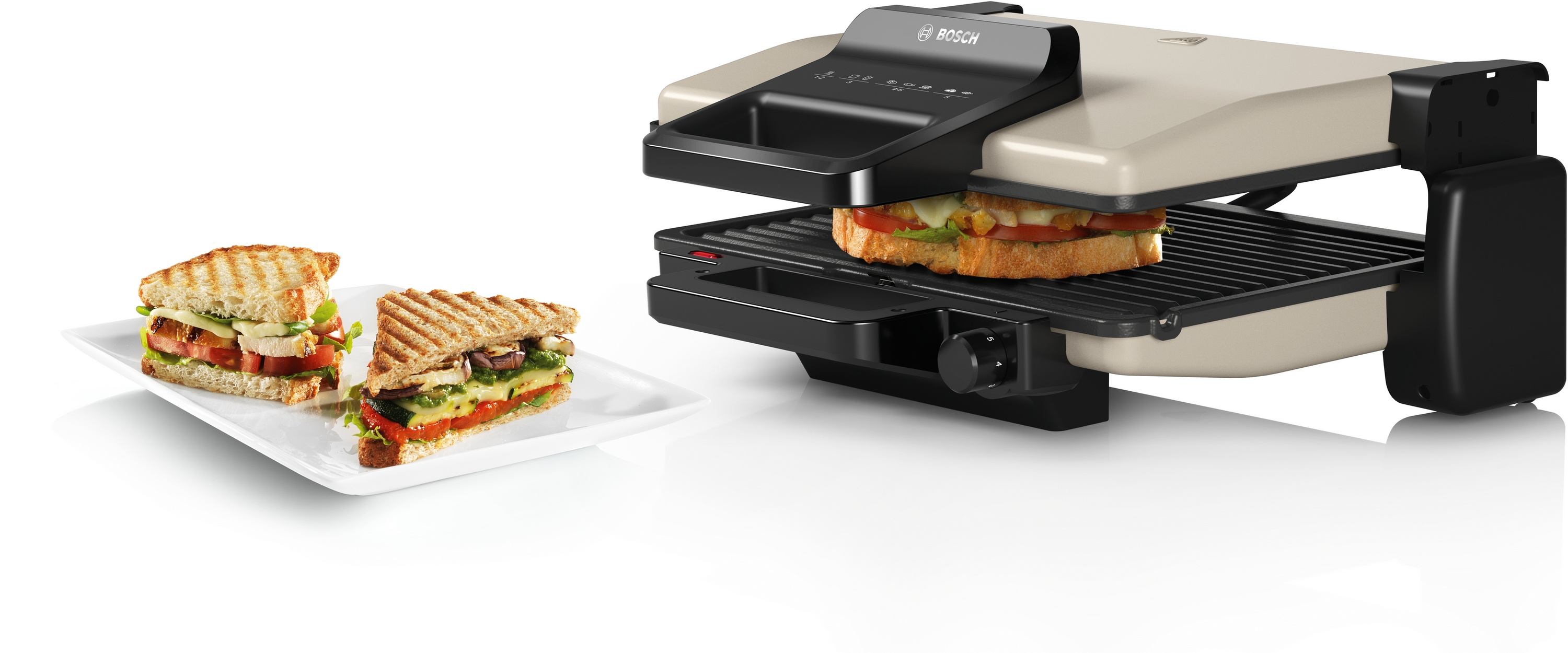 Ein Sandwichmaker mit zwei Sandwiches, eines darin und eines auf einem Teller.