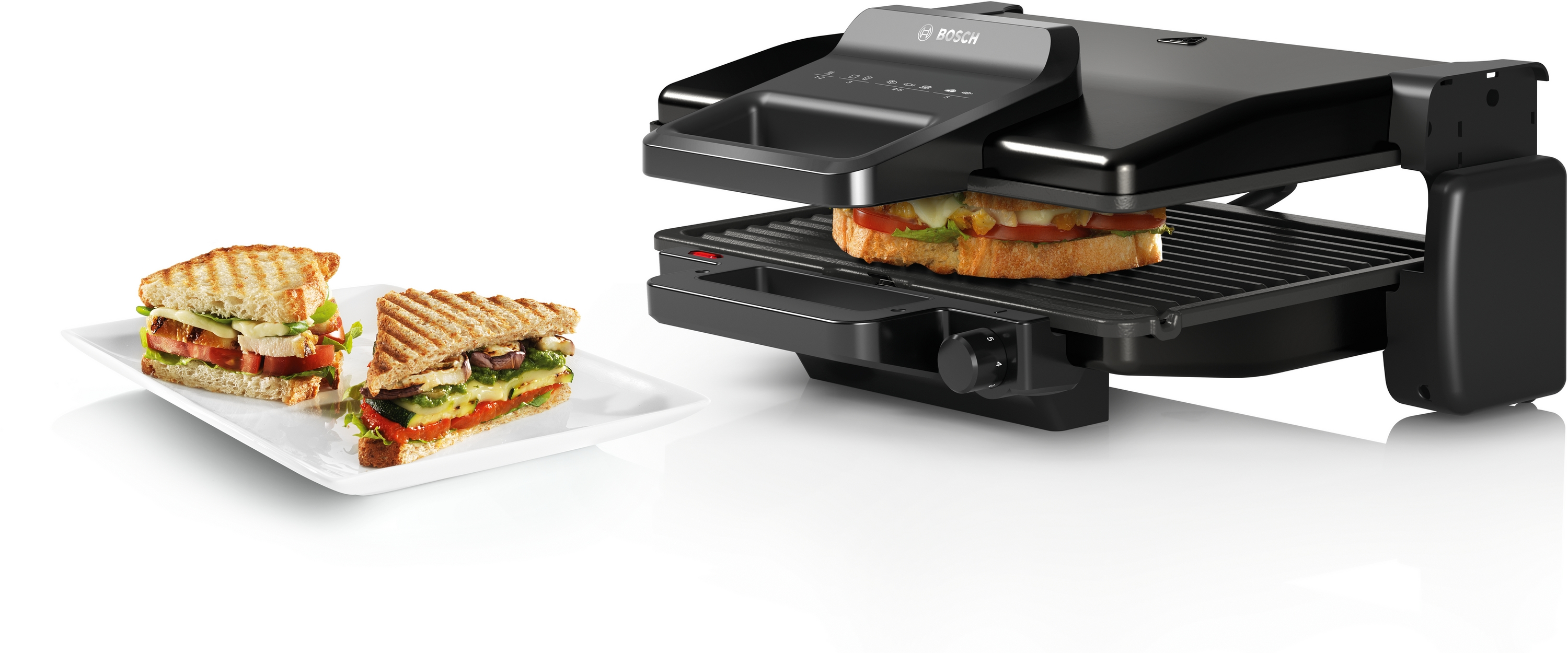 Ein schwarzer Kontaktgrill mit zwei Sandwiches, einer darin und einer daneben.