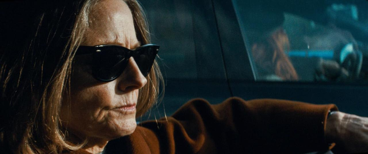 Eine Frau mit Sonnenbrille sitzt im Auto, ihre Hand ruht auf dem Lenkrad.