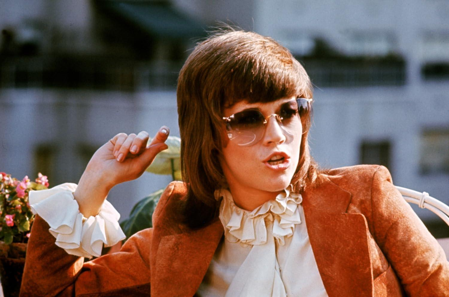 Eine Frau mit braunen Haaren und Sonnenbrille trägt einen orangefarbenen Blazer.