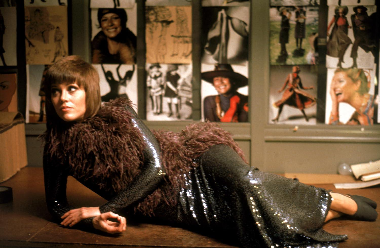 Frau in Glitzerkleid und Federboa liegt auf einem Tisch, im Hintergrund Bilder.