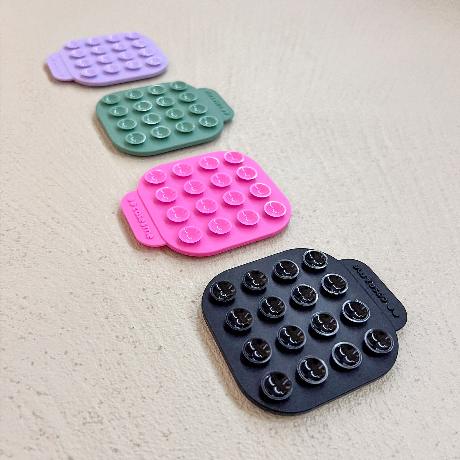 Four suction cup mounts in purple, green, pink, and black on a light gray surface.