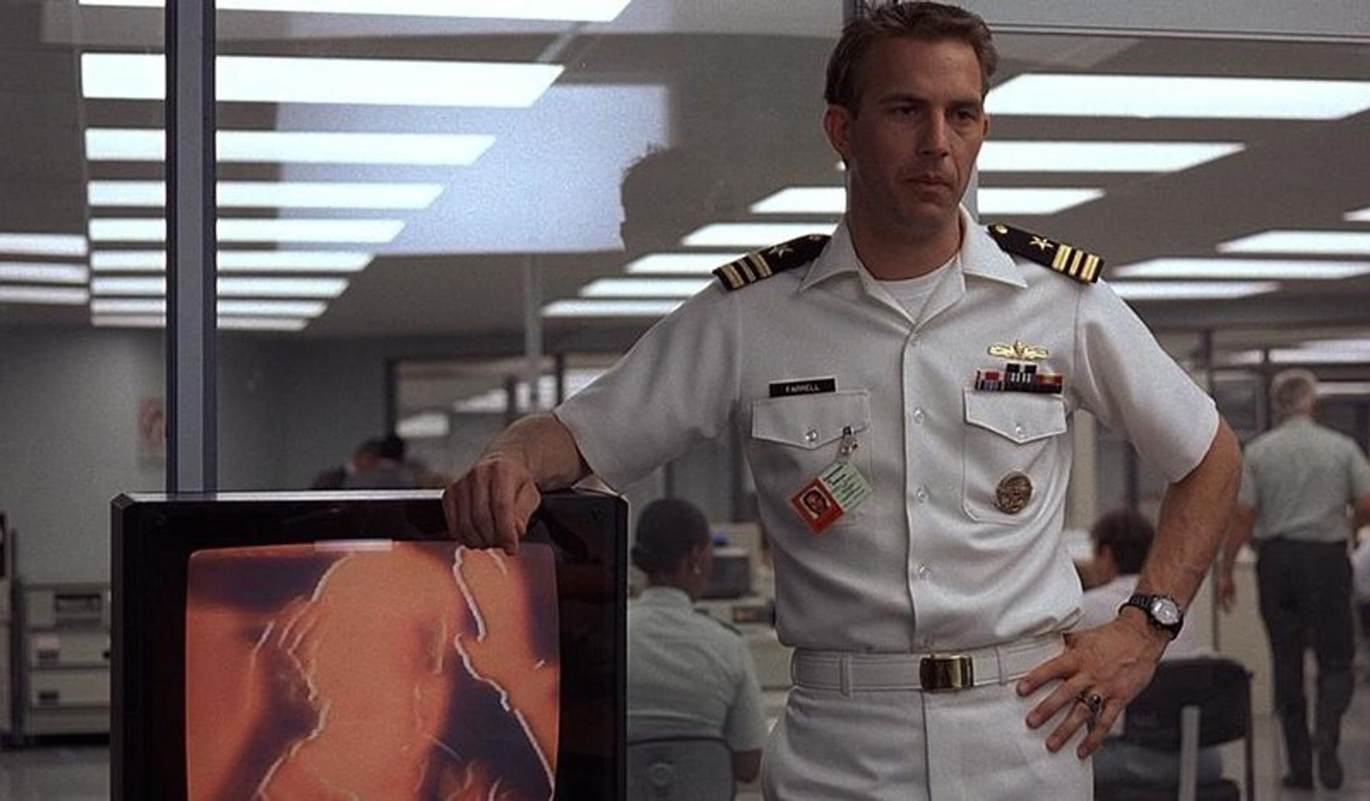 Ein Mann in Uniform steht neben einem Monitor mit einem orangefarbenen Bild.