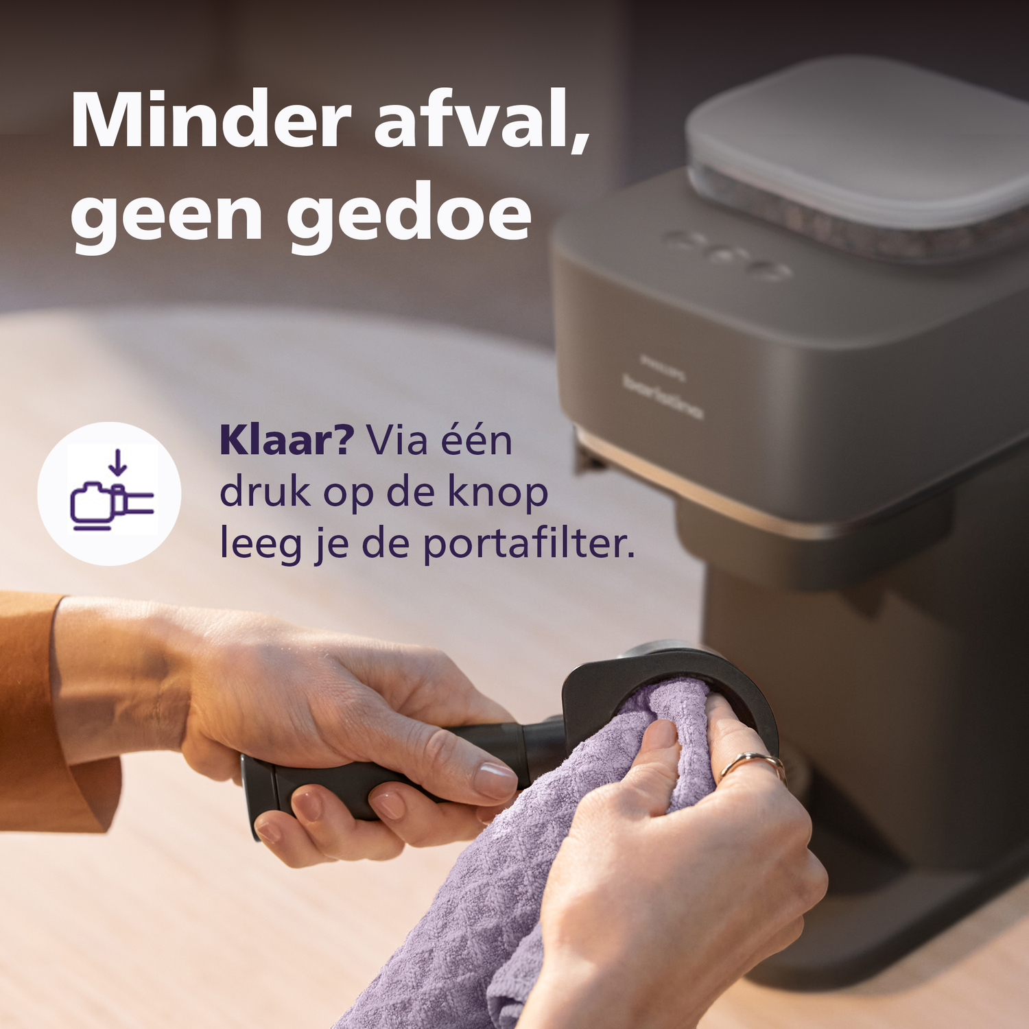 Een hand reinigt een portafilter met een doek naast een koffiezetapparaat.