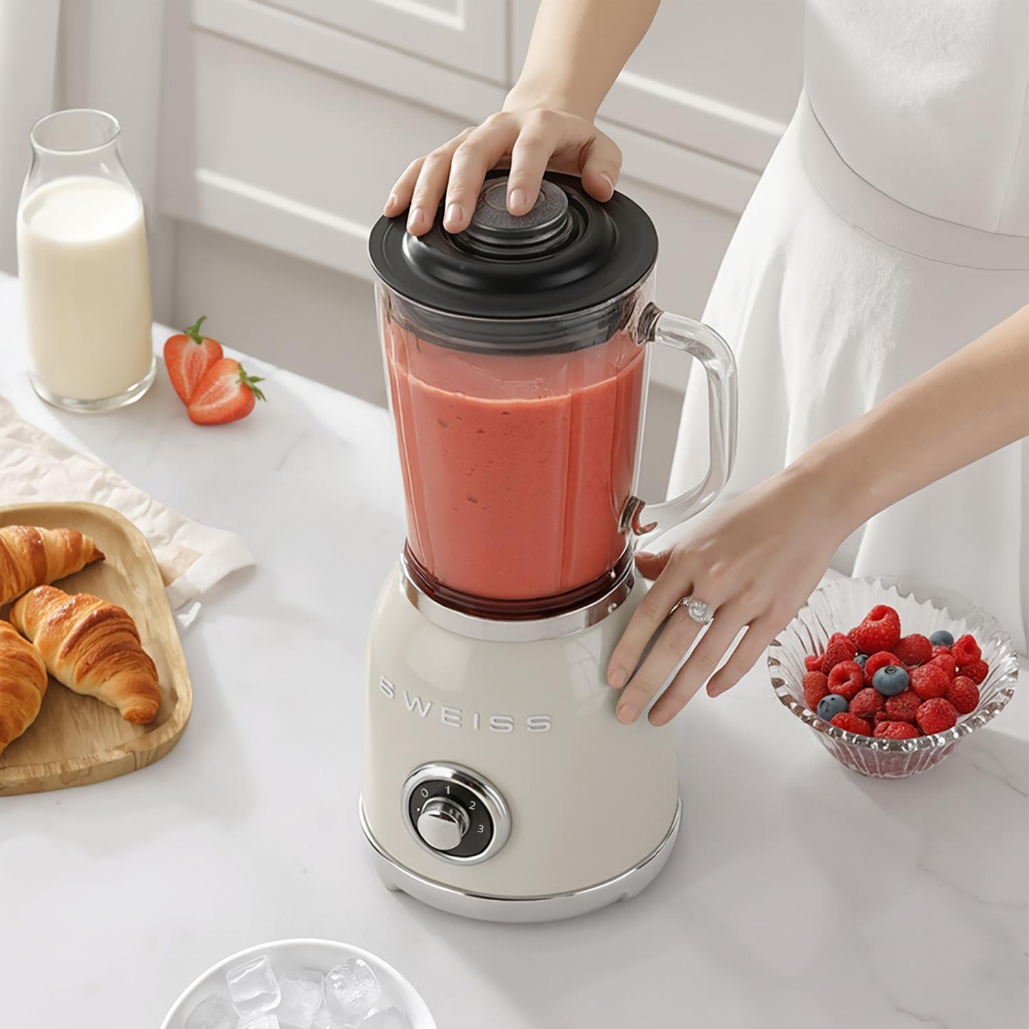 Una persona usa un frullatore con frullato rosso, accanto a bacche, croissant e latte.