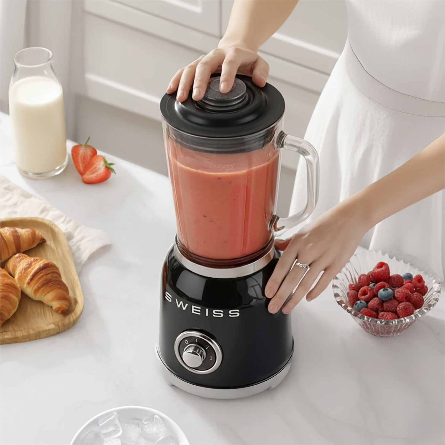 Un frullatore nero con frullato rosso, vicino a croissant, latte e frutti di bosco.