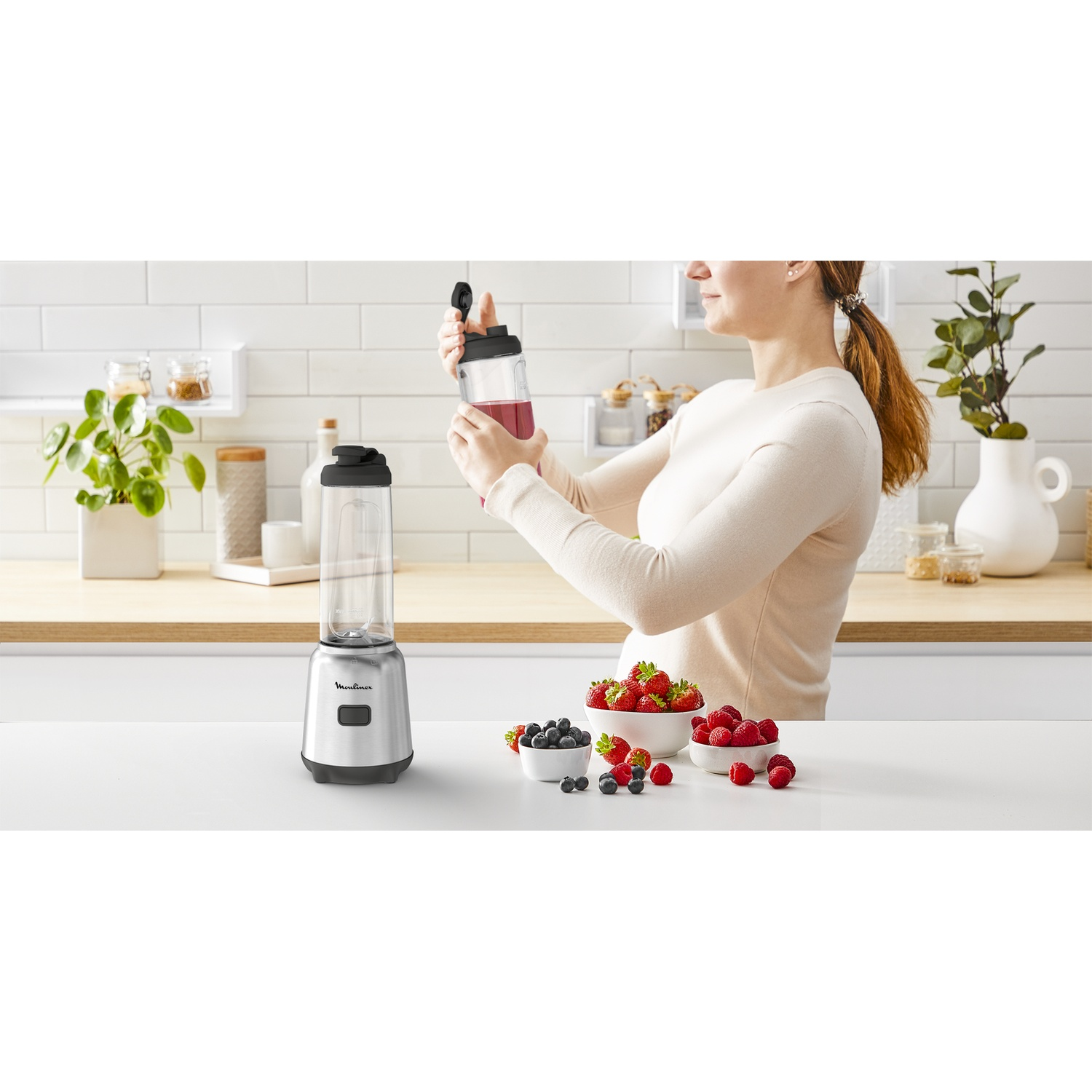 Donna prepara frullato con frullatore e frutti di bosco freschi in cucina luminosa.