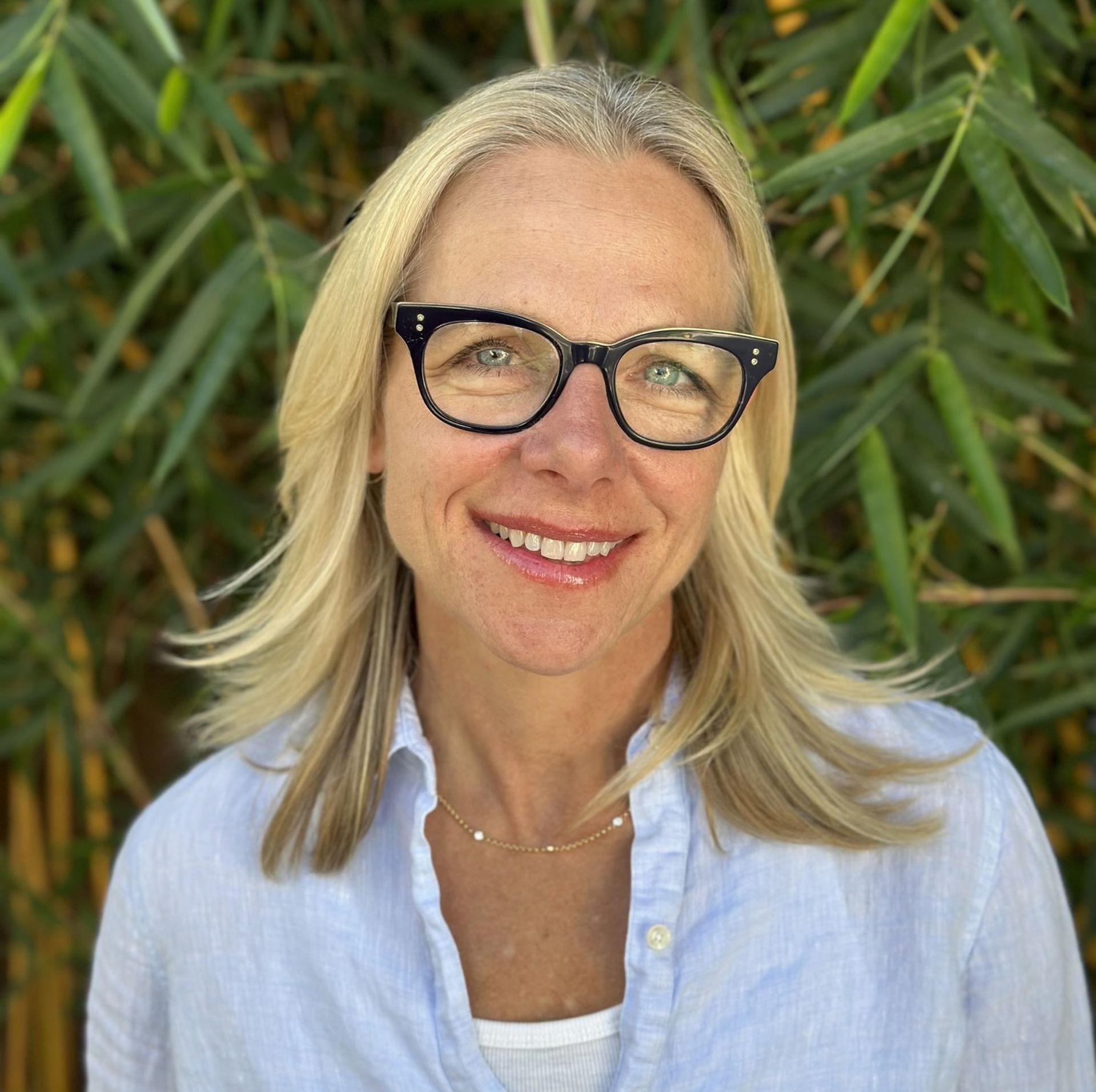 Eine Frau mit blonden Haaren und Brille lächelt vor Bambus.
