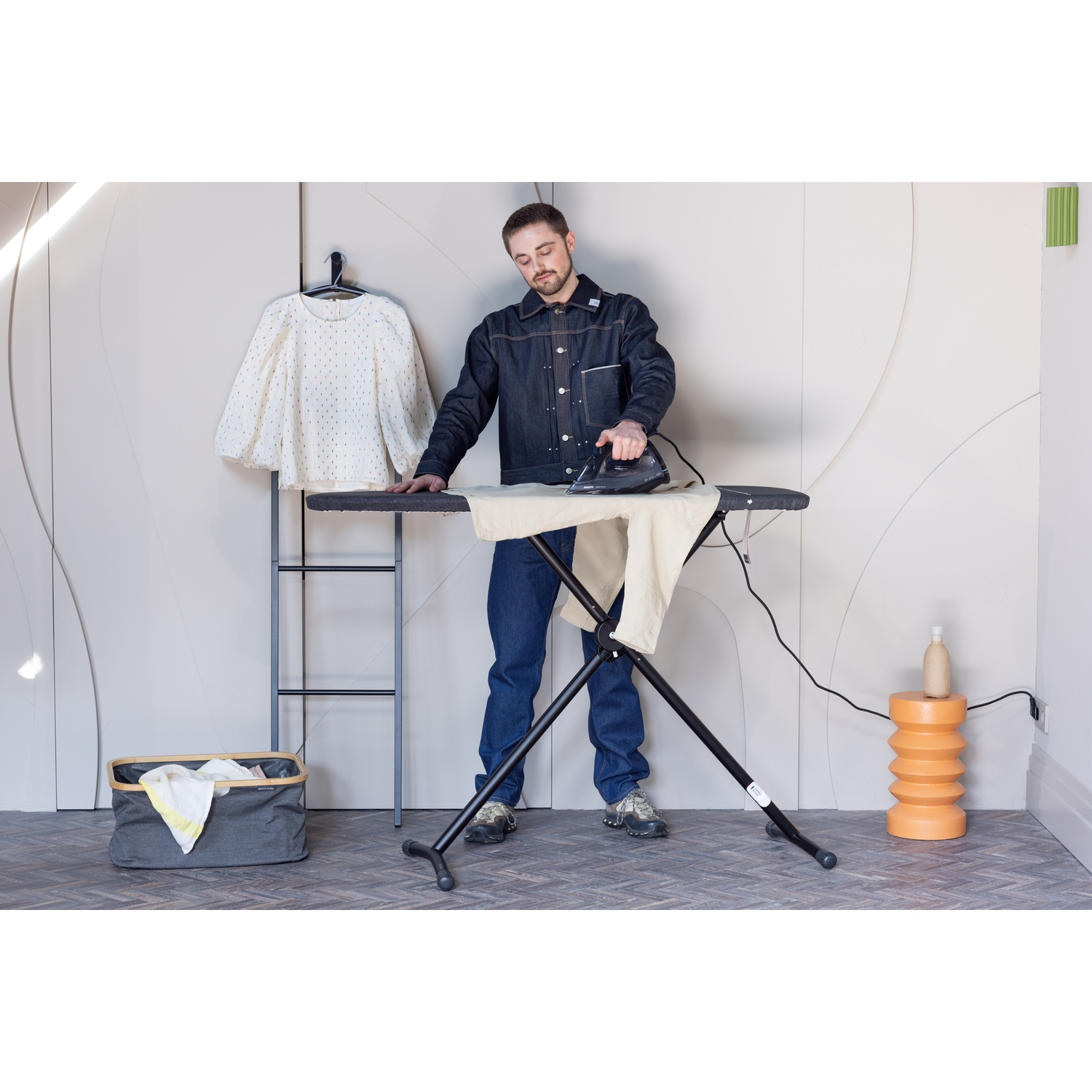 Man strijkt kleding op een plank. Wasbak en shirt in de buurt.