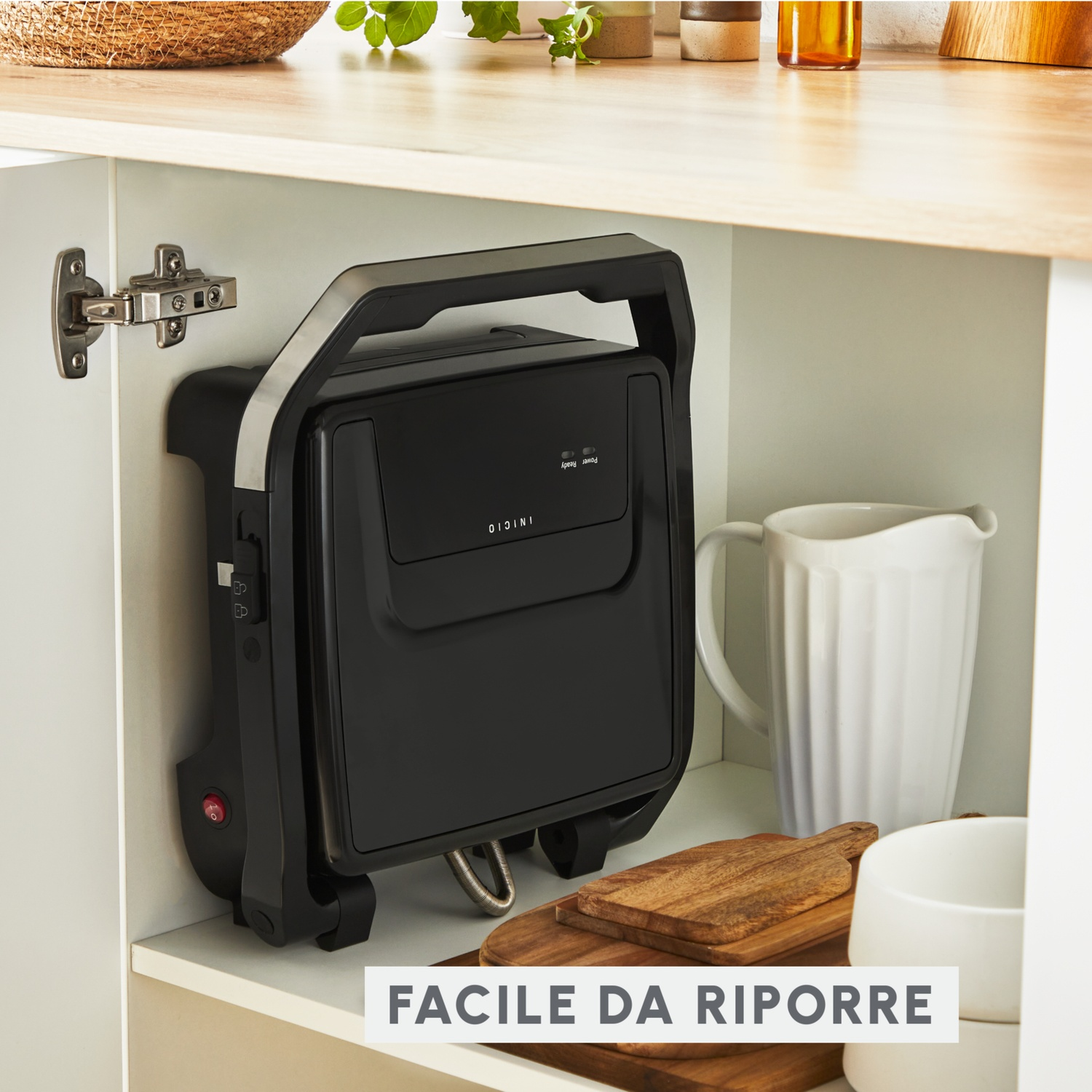 Tostiera per panini nera riposta in verticale su mensola con brocca bianca e taglieri.